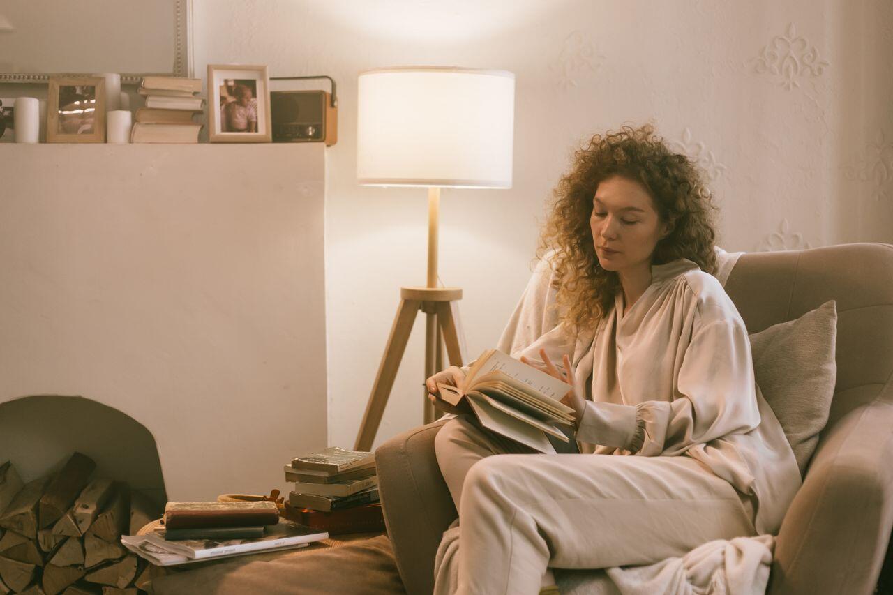 jeune femme aux cheveux boucles assise sur un fauteuil avec une lampe et lisant