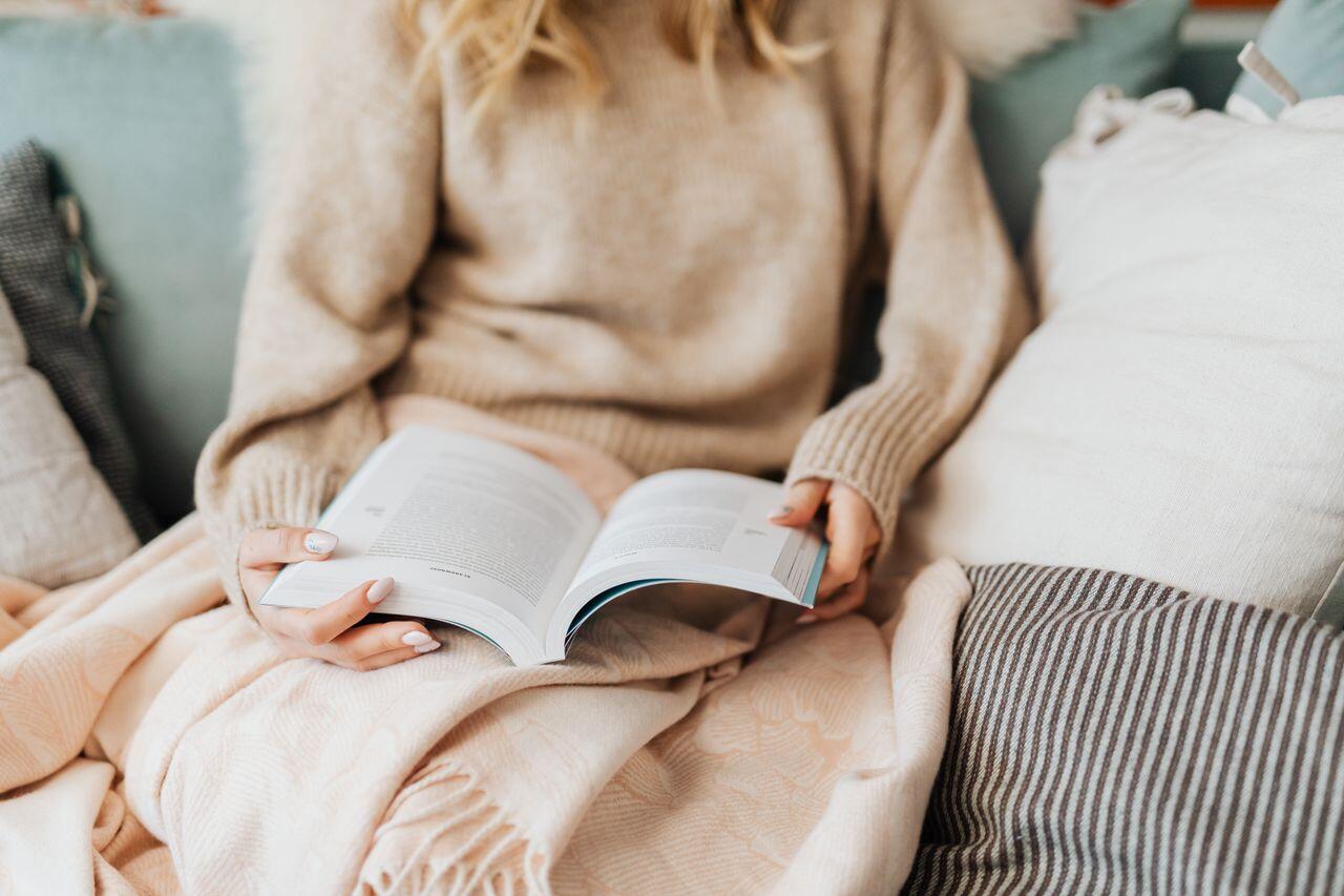 jeune femme assise en beige avec un plaid lisant son livre