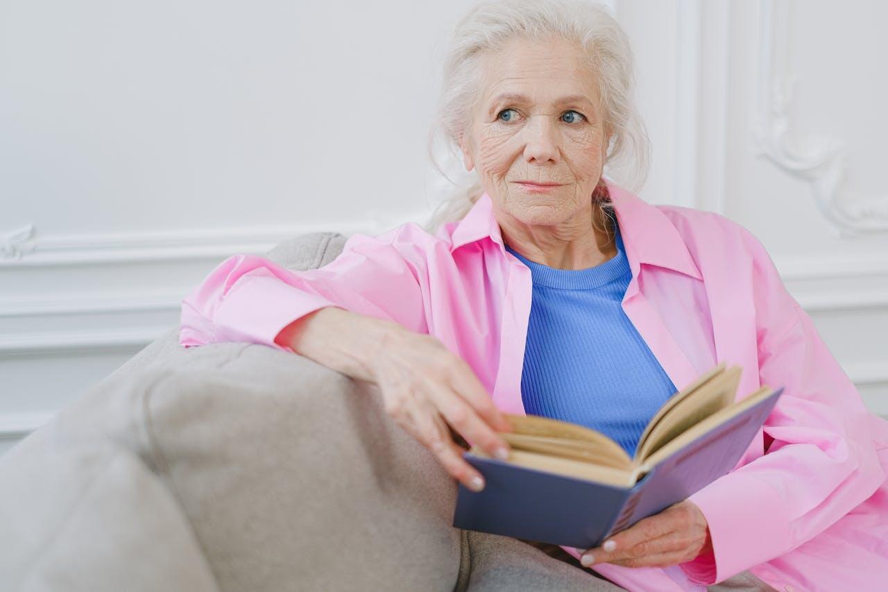 femme agee en rose lisant sur le canapé