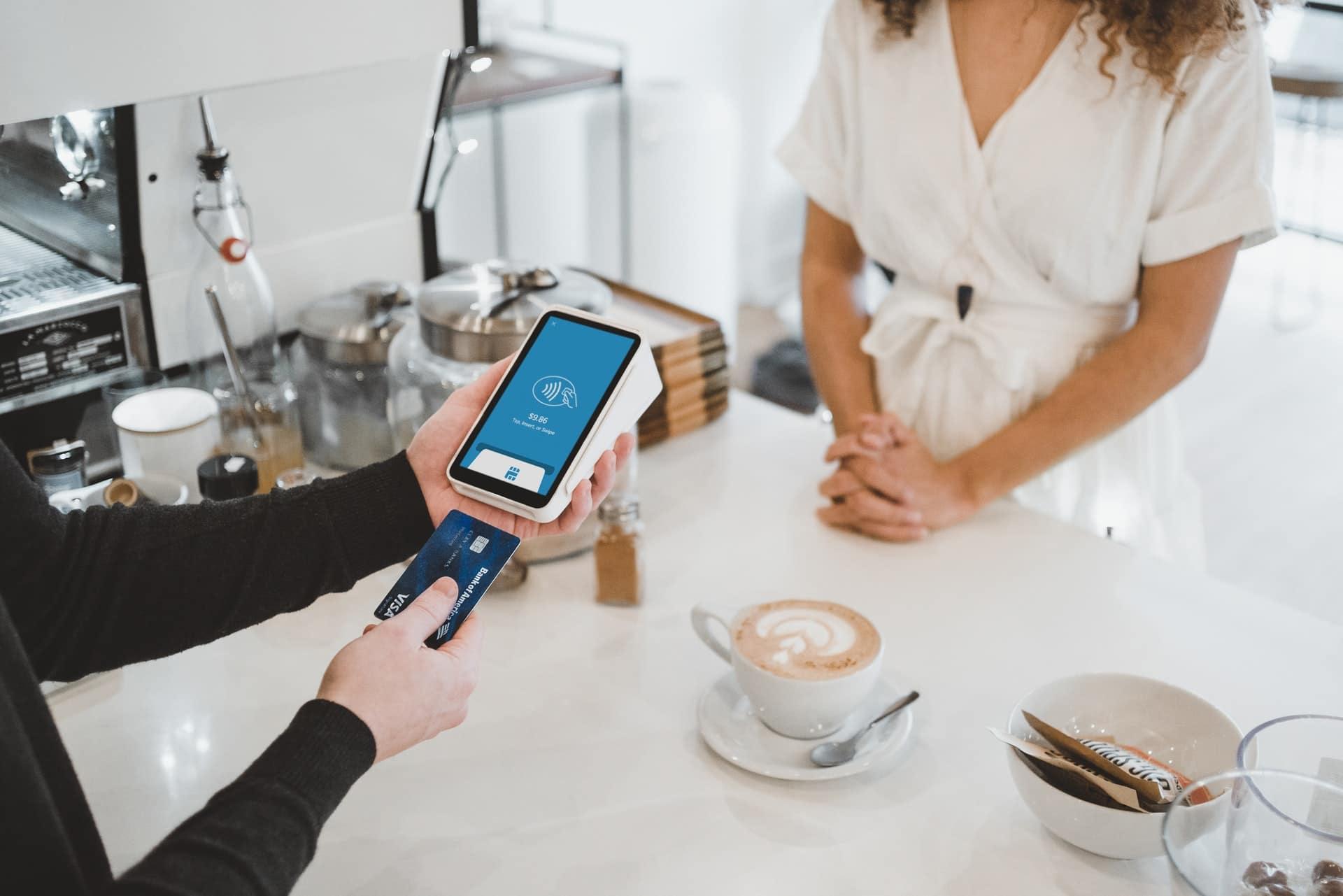 homme dans sa cuisine avec un cappuccino utilisant un lecteur de carte bancaire