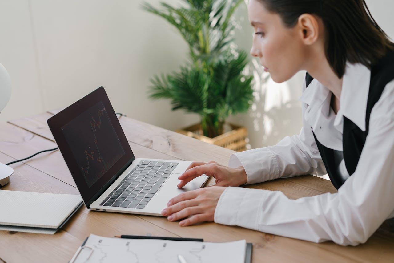 jeune femme sur une table travaillant sur sonordi avec stylo et feuille a cote