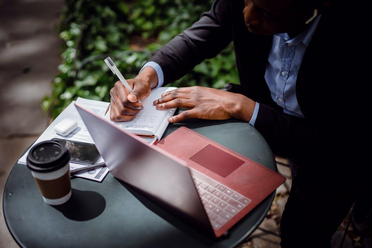 homme avec son ordi et son carnet sur une table dehors