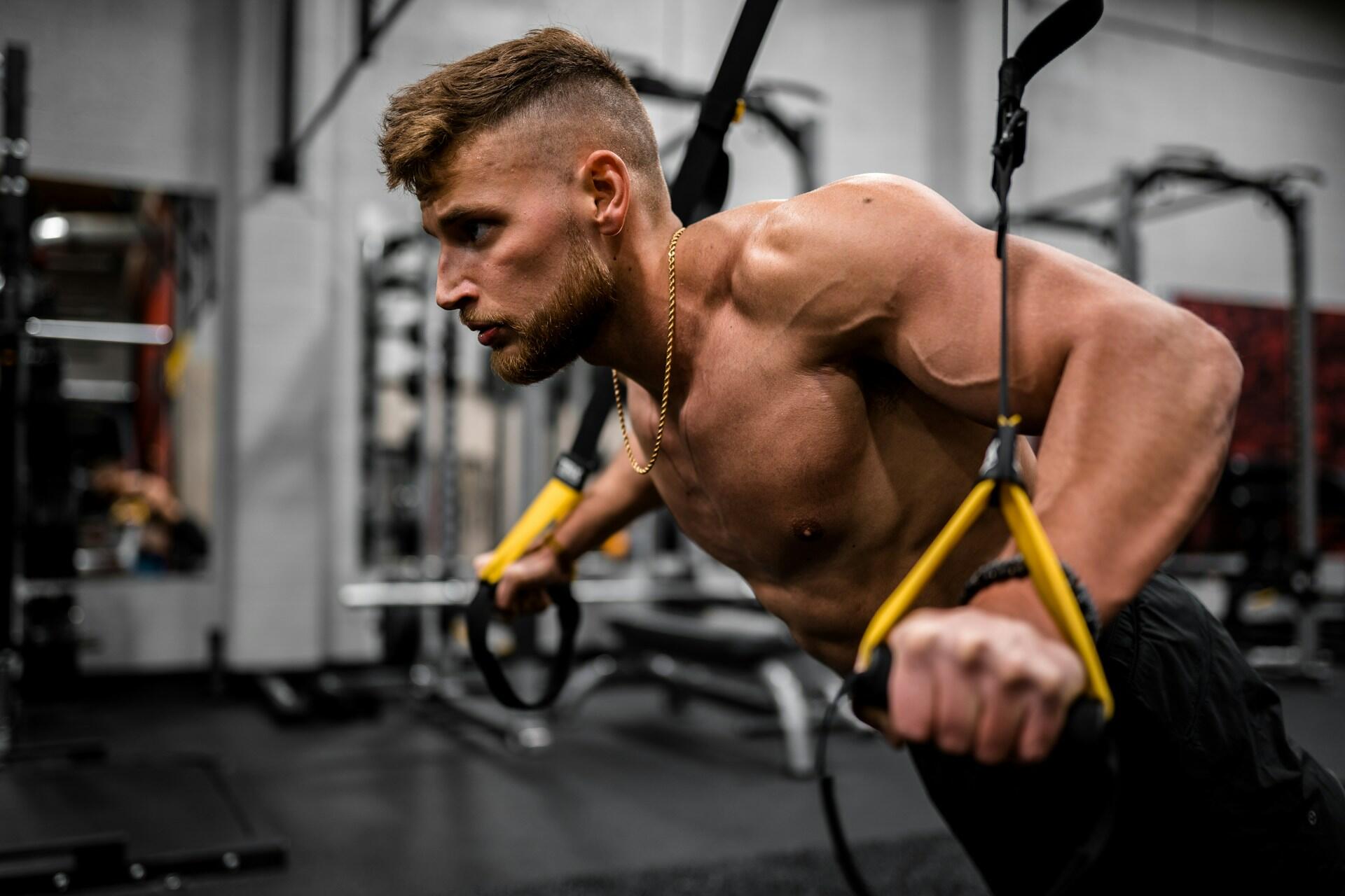 homme torse nu en muscle utilisant les trx