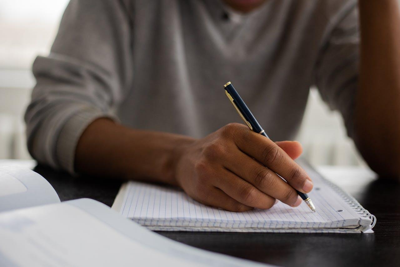 homme ecrivant dans un cahier sur une table pour etudier
