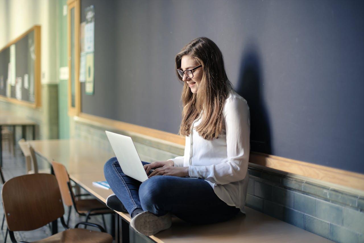 jeune ado avec son laptio assise sur une table contre un tableau noir
