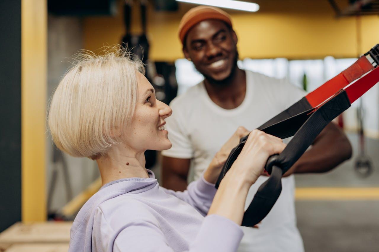 femme blonde faisant du trx avec coach derriere qui la soutient