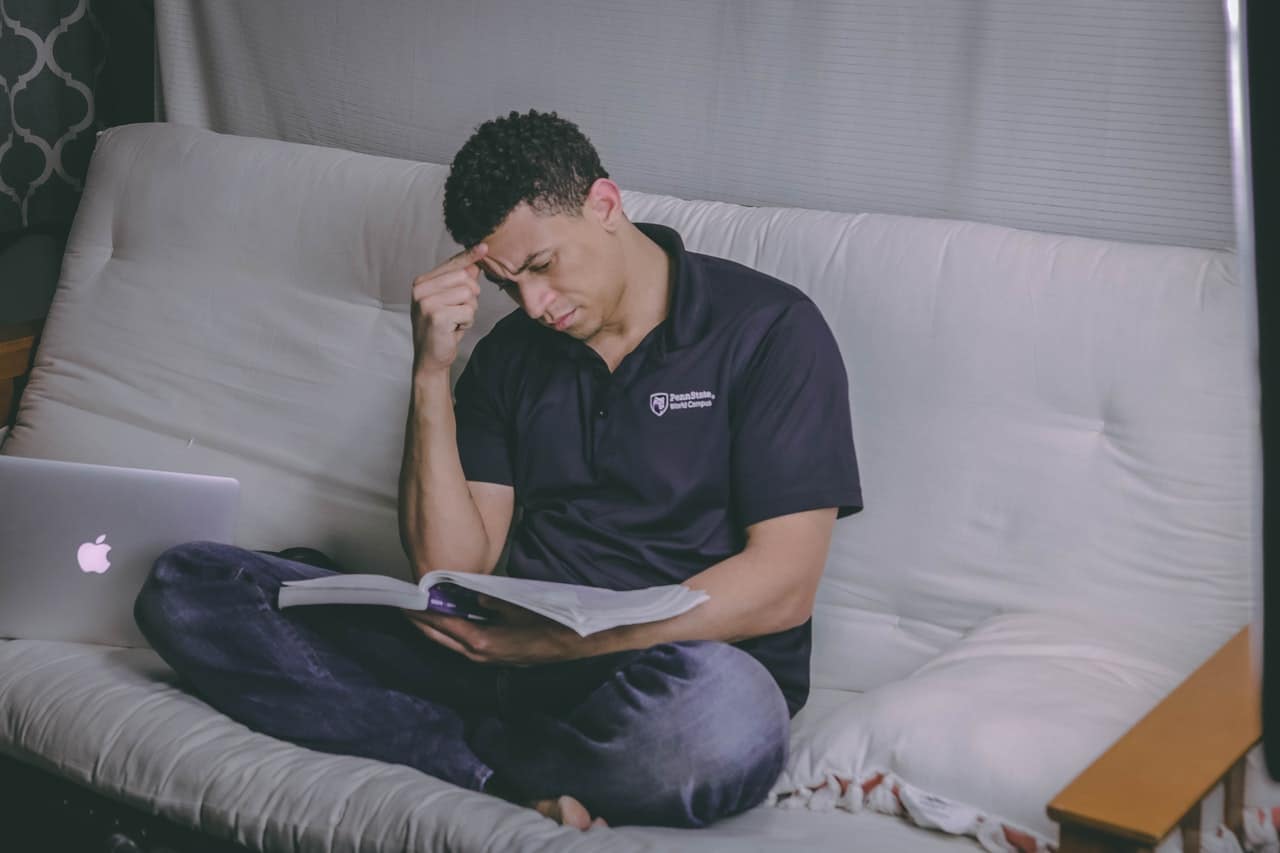 homme étudiant un bouquin sur son lit