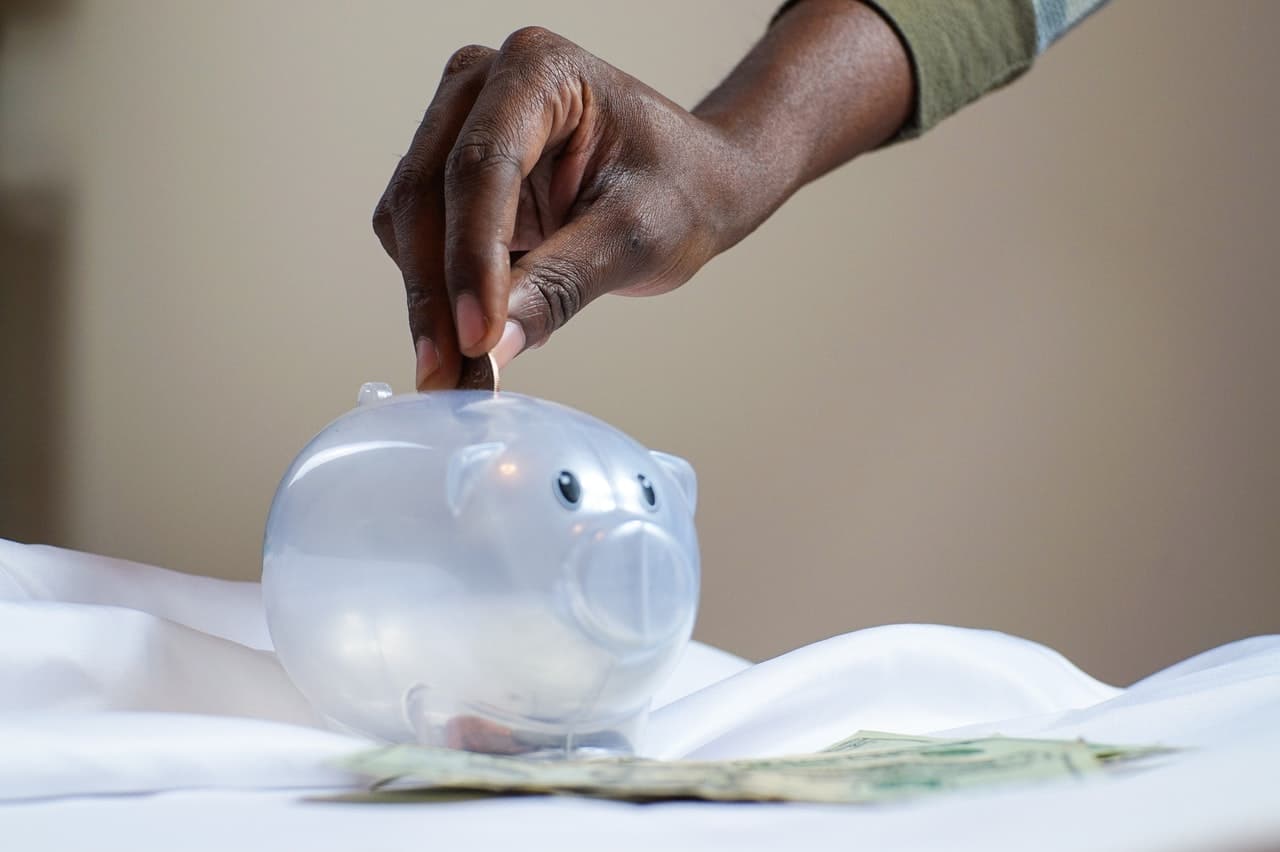 main mettant une piece dans une tirelire cochon en plastique transparente 
