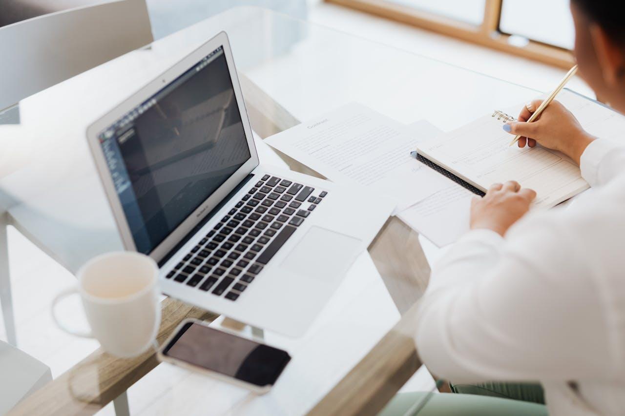 personne travaillant sur une table avec laptop et papiers eparpilles