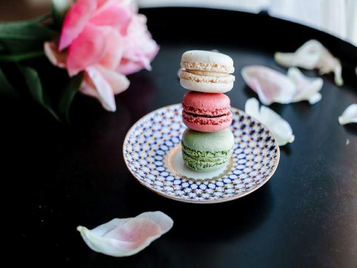 Mini-macarons à la pistache, à la framboise et la vanille empilés dans une petite assiette et entourés de pétales de roses