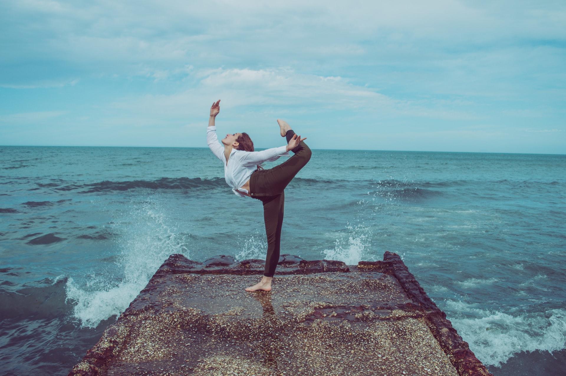femme effectuant une posture de danse devant l'océan