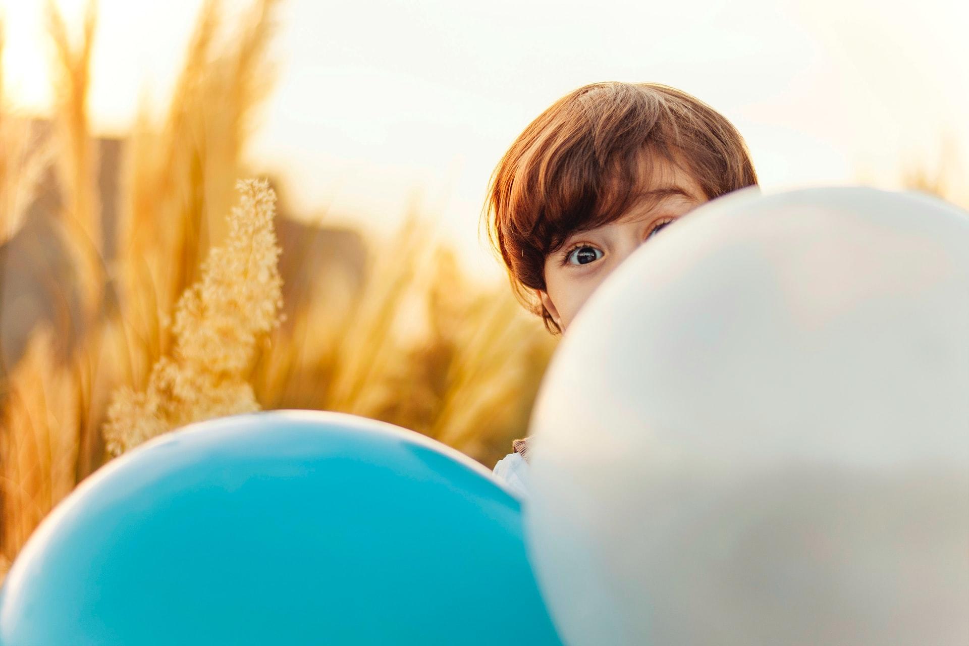 petit garçon dans les champs de blé se cachant derrière les ballons