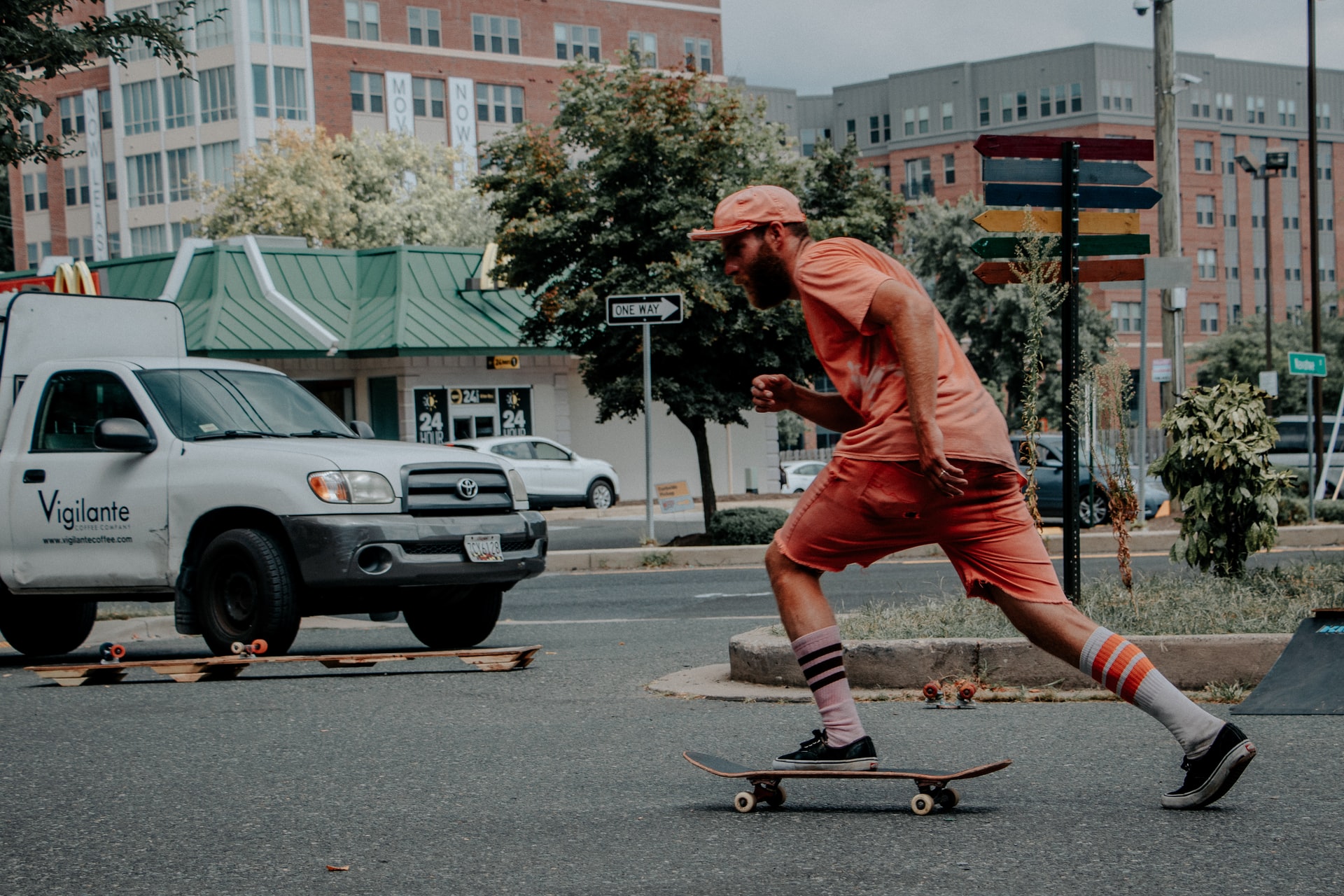 Homme habillé en orange se déplaçant avec son skate sur la route