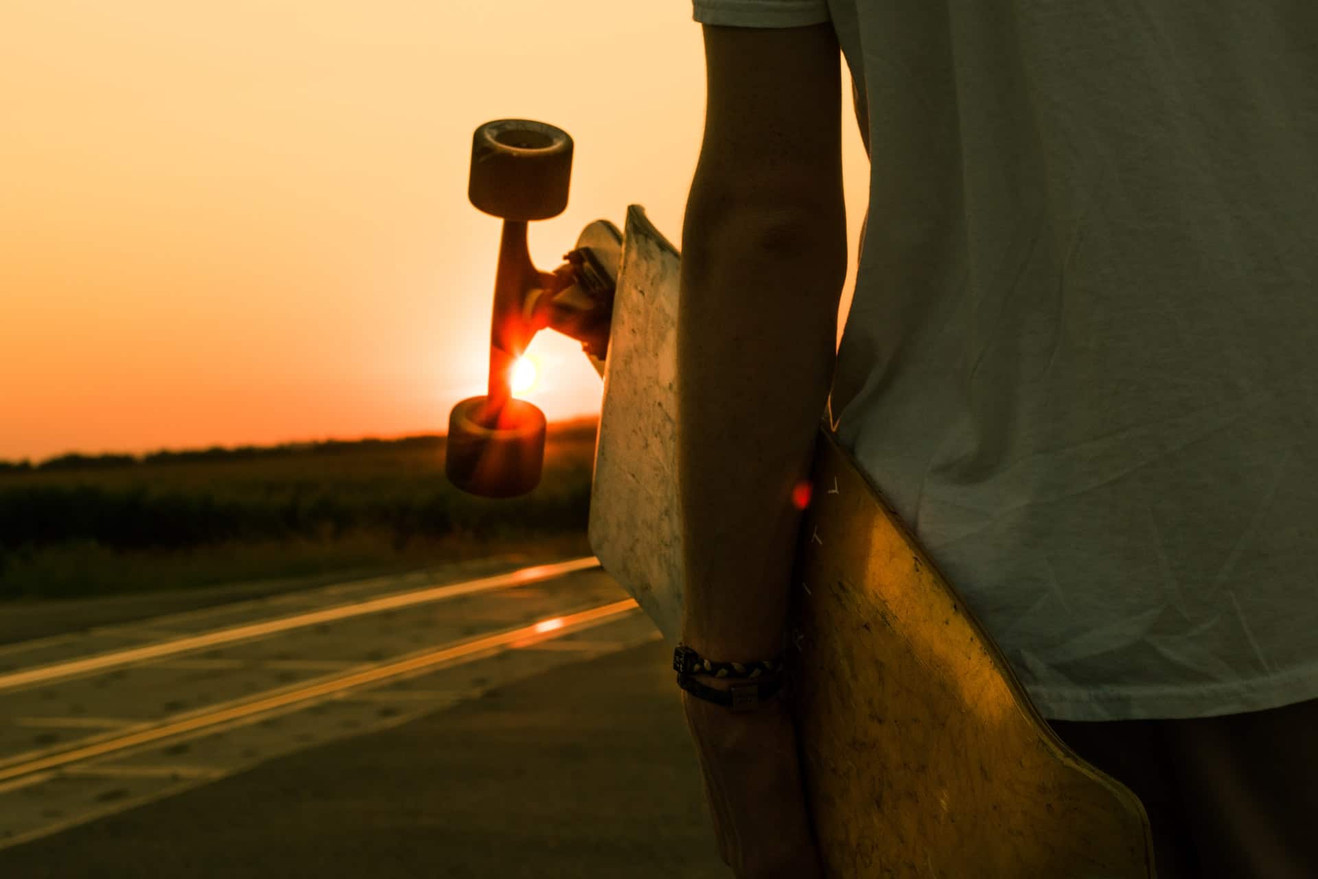 jeune portant son skate au coucher du soleil