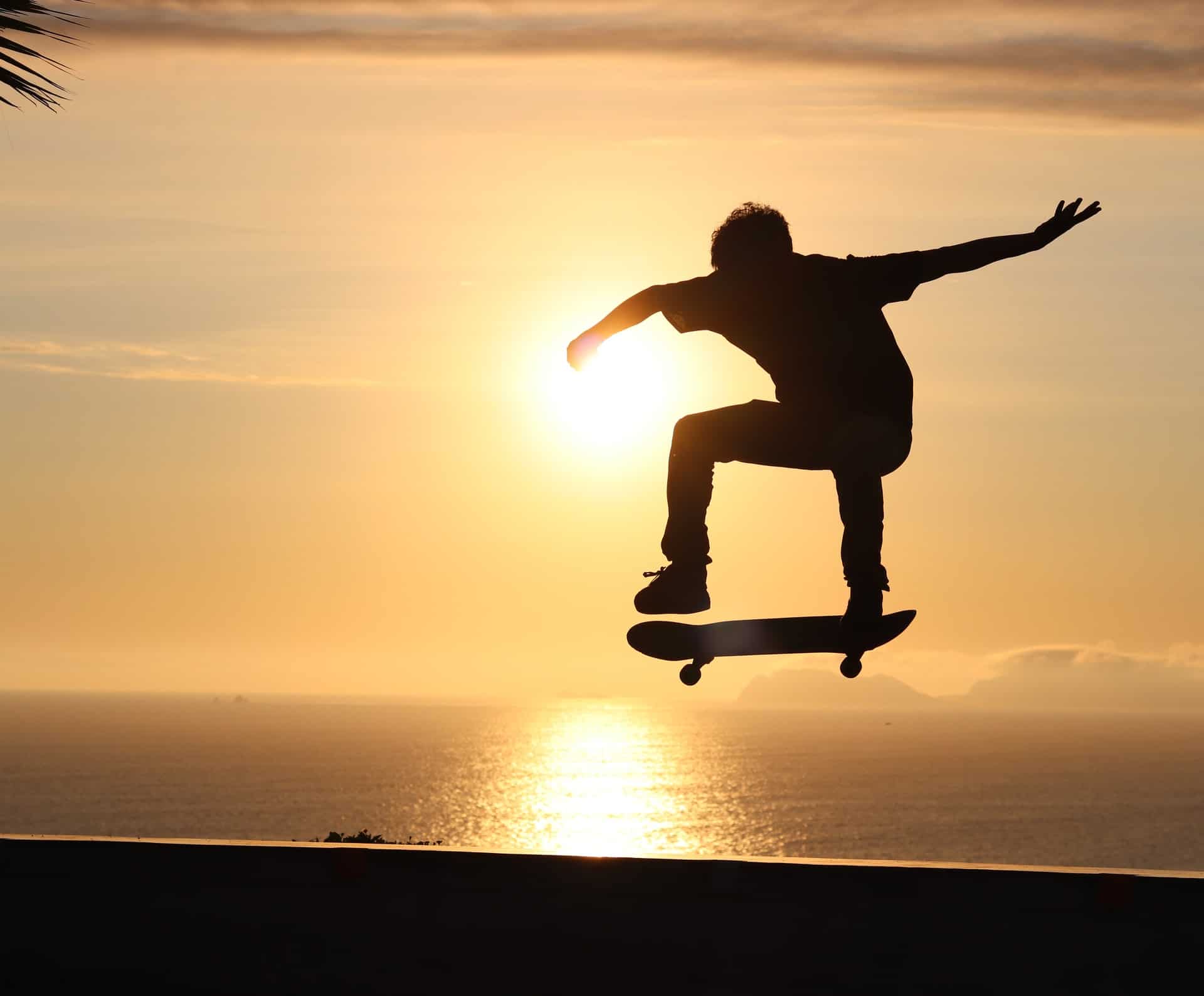jeune effectuant un saut avec son skate face à la mer et au coucher du soleil