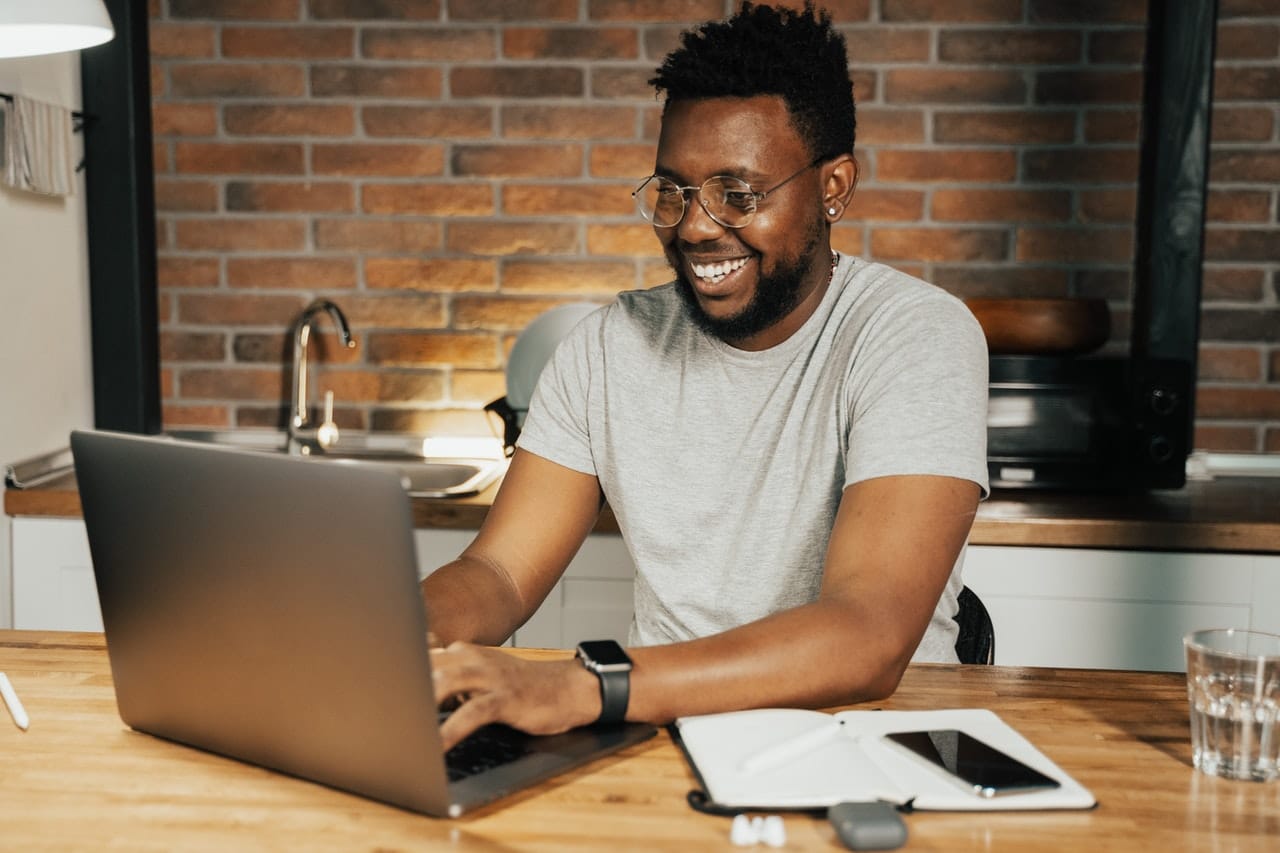 jeune homme souriant travaillant sur son laptop dans la cuisine