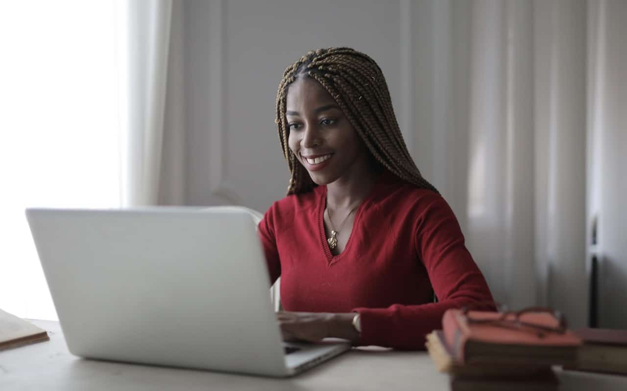 jeune femme en pull rouge souriante derrière son laptop