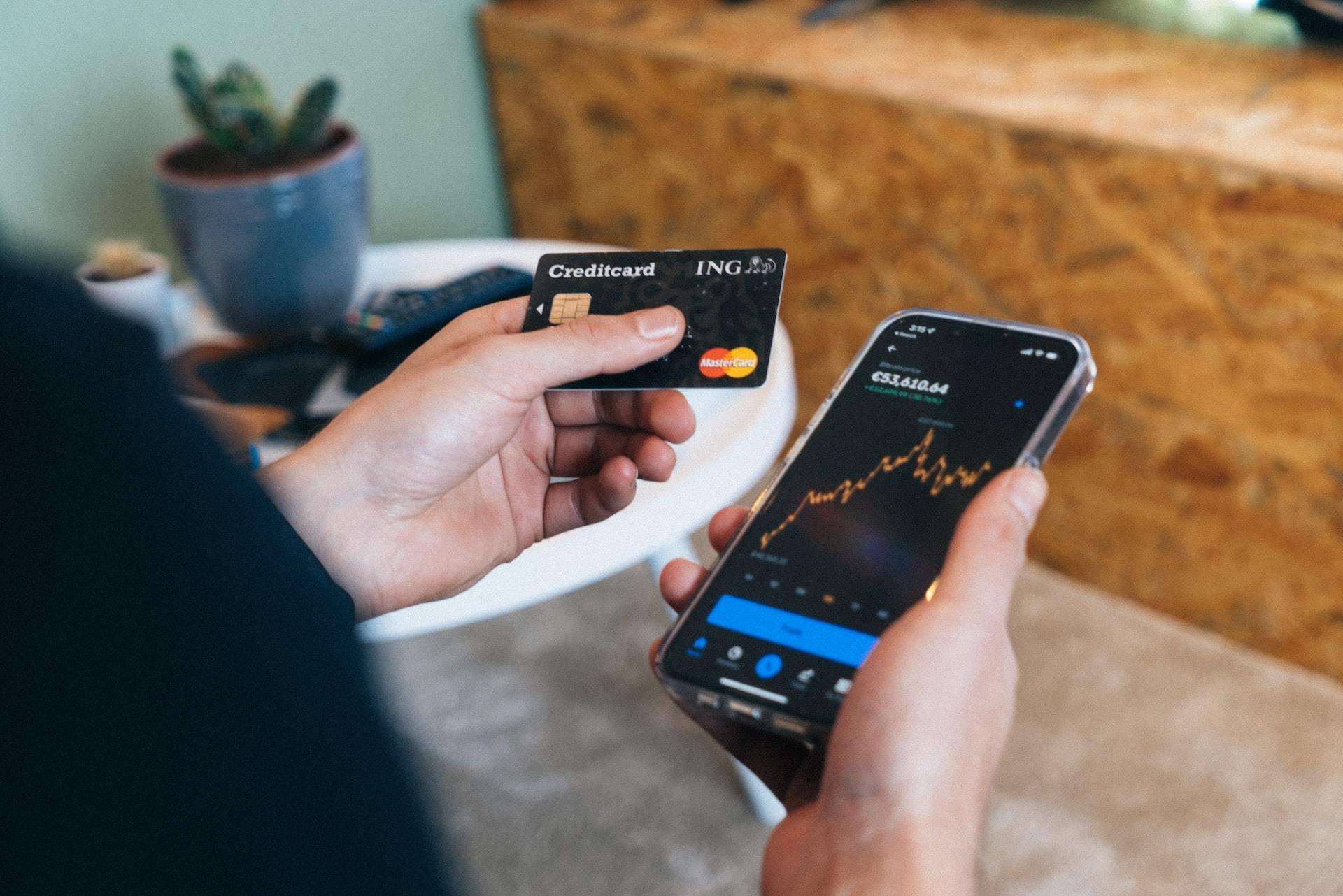 personne tenant une carte de credit et un telephone avec une courbe