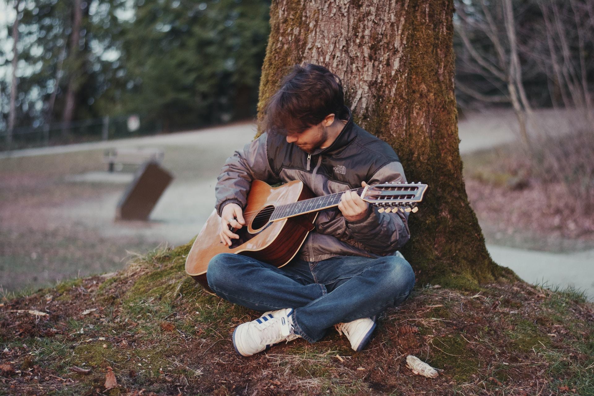 Un guitariste assis au pied d'un arbre.