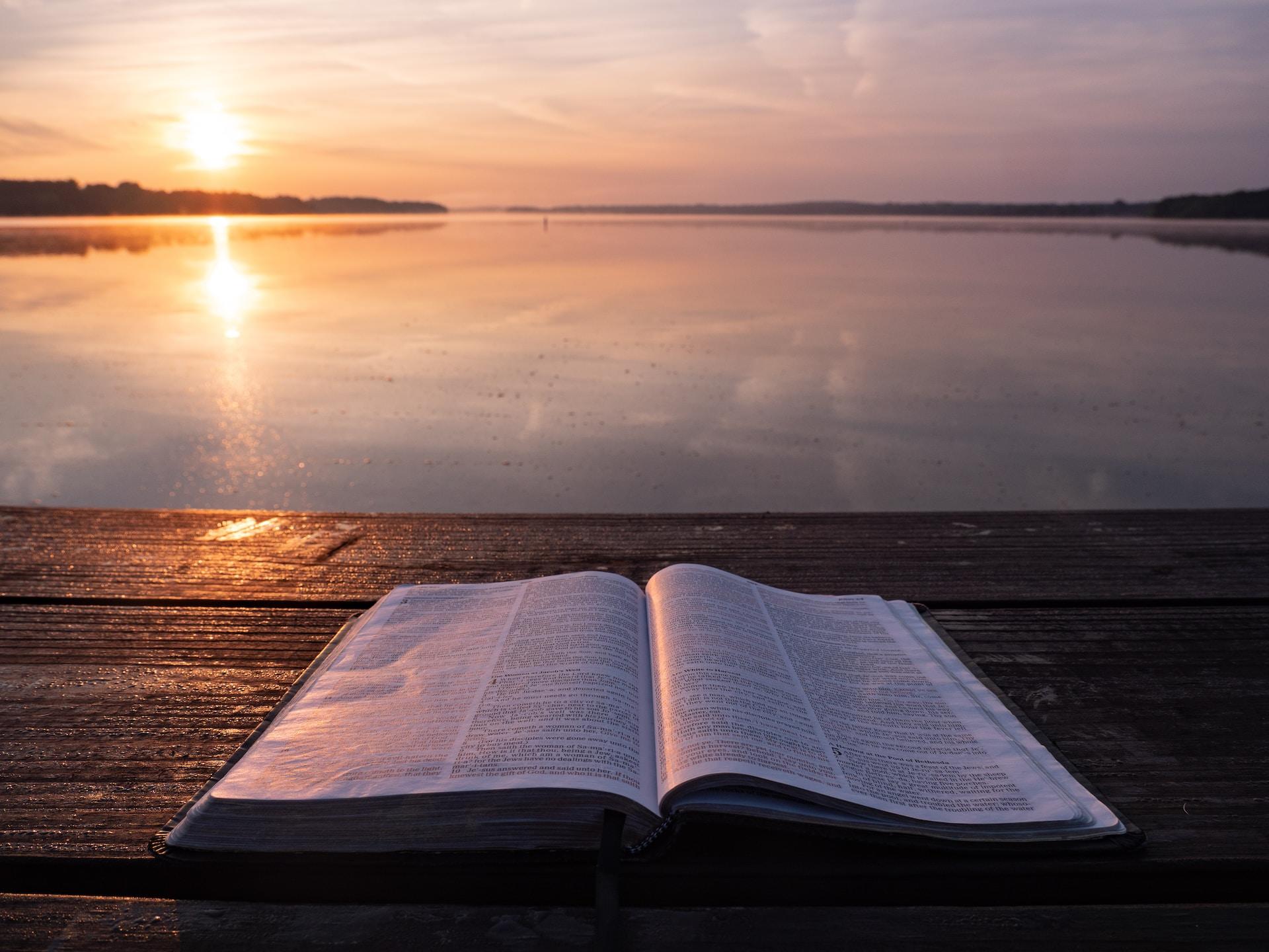 livre posé sur une table en bois face à un coucher de soleil