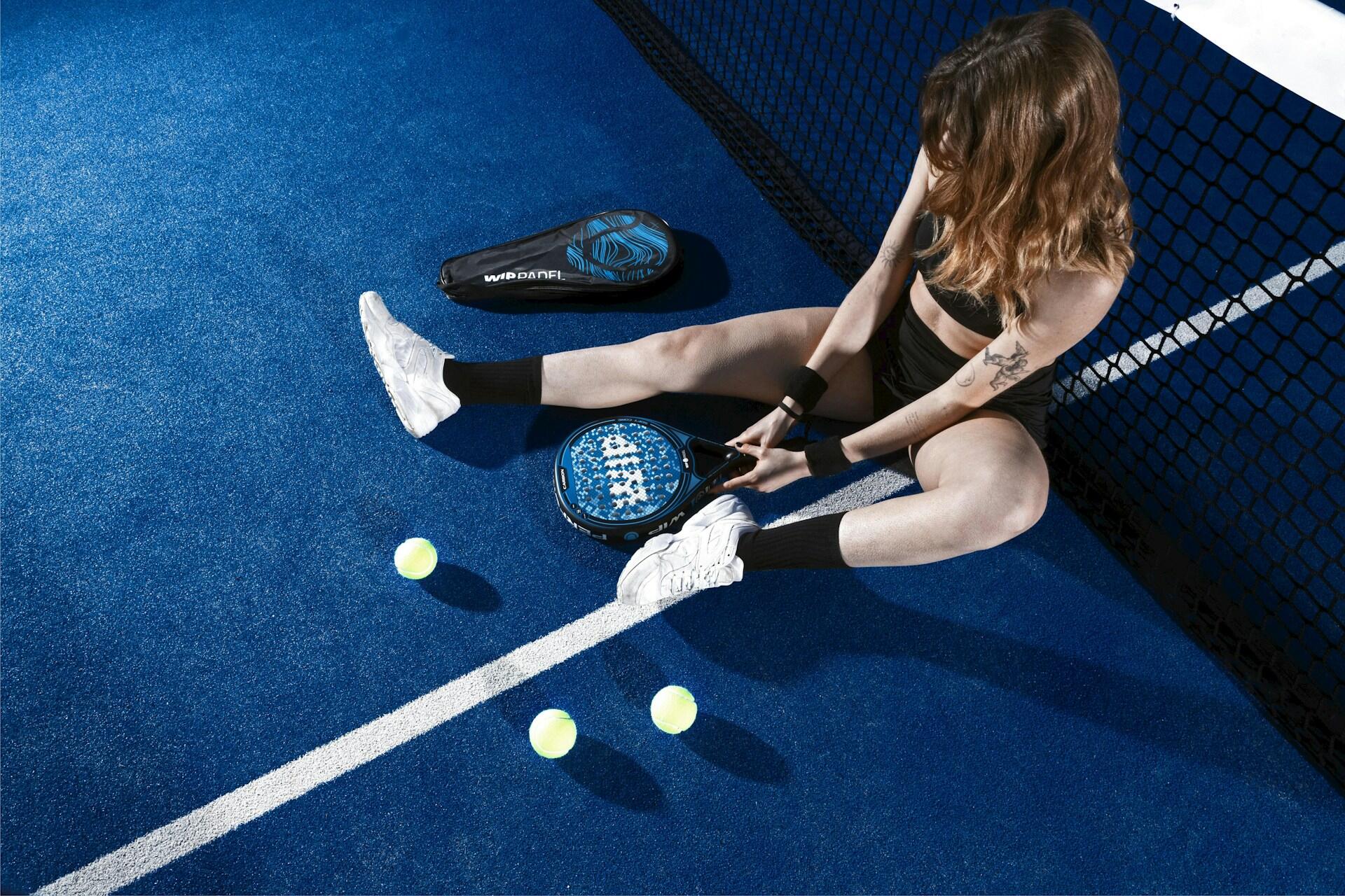 joueuse de padel assise sur le terrain entouree de raquettes bleues et de balles jaunes