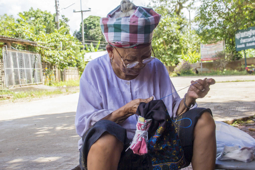 Mujer anciana cociendo en la calle