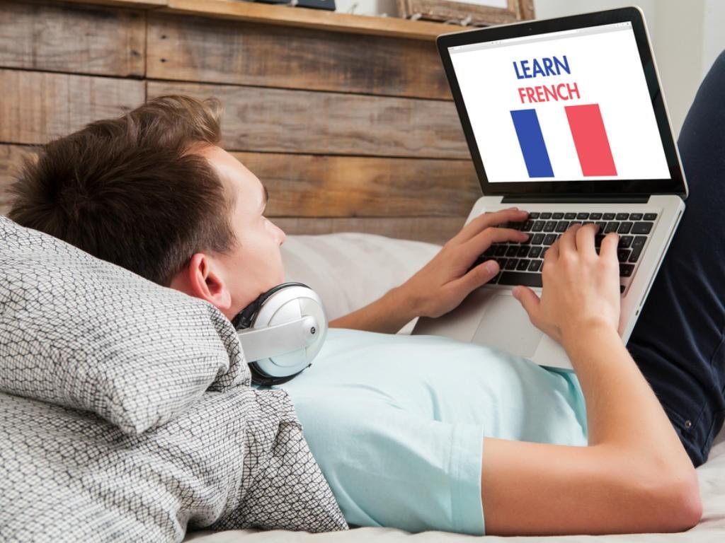 Estudiante reclinado en su cama aprendiendo francés en su computadora