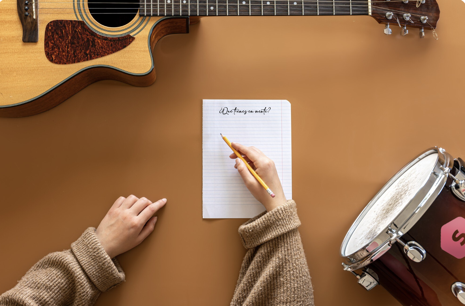 vista cenital de una mano frente a una libreta vacia con guitarra y bongós alrededor
