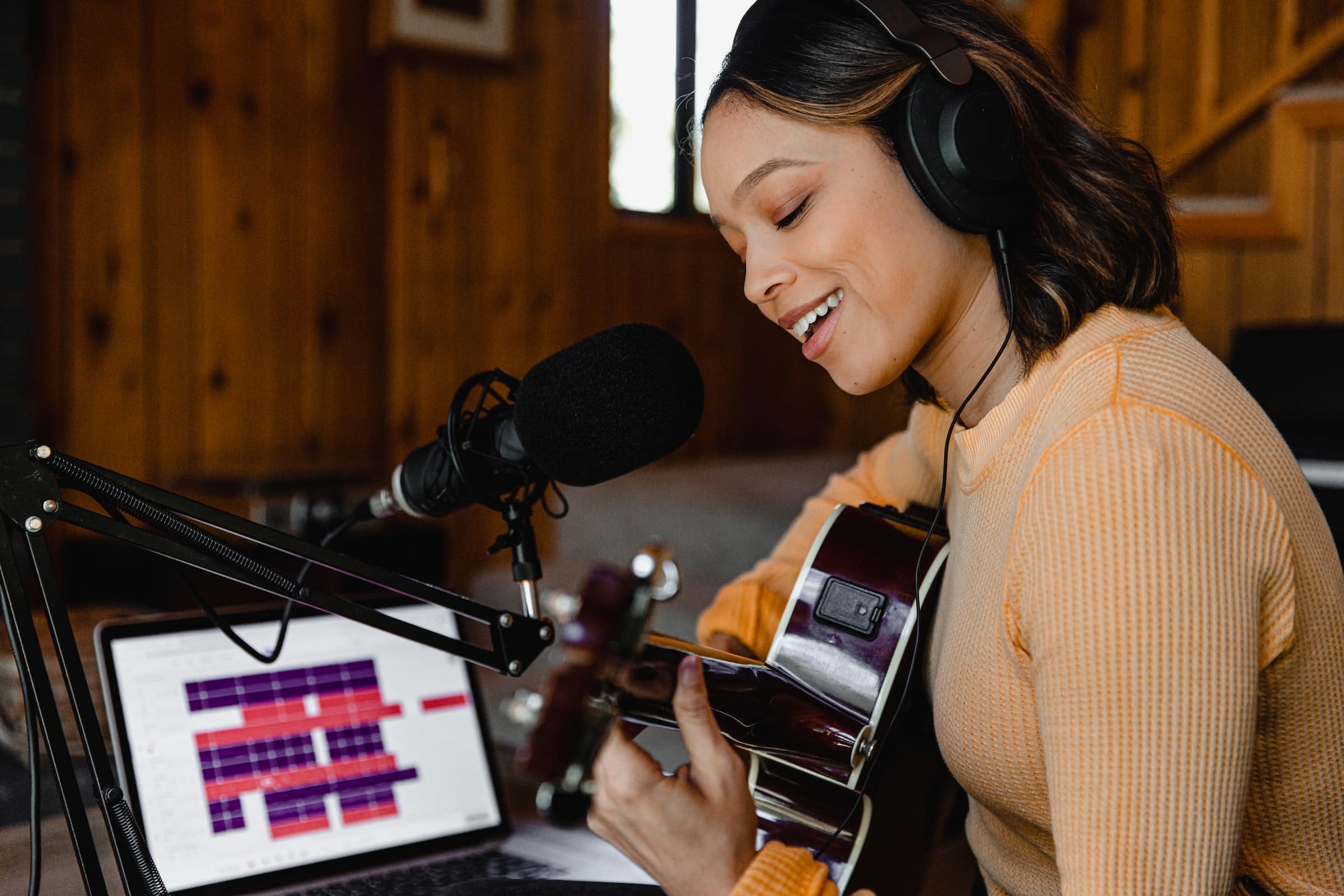 Cantante mujer sonriente grabando con guitarra y laptop