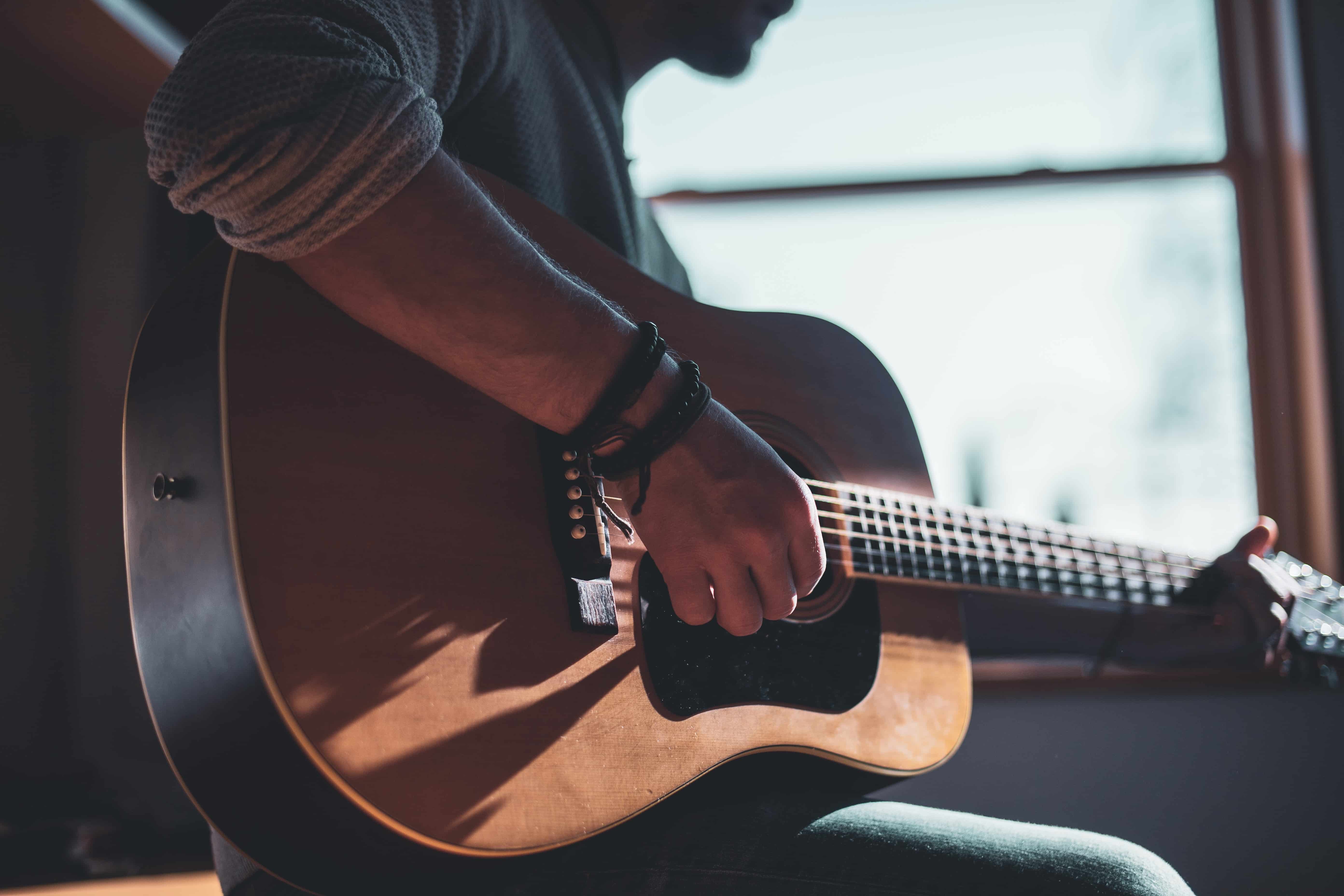 chico tocando una guitarra sentado de lado frente a una ventana