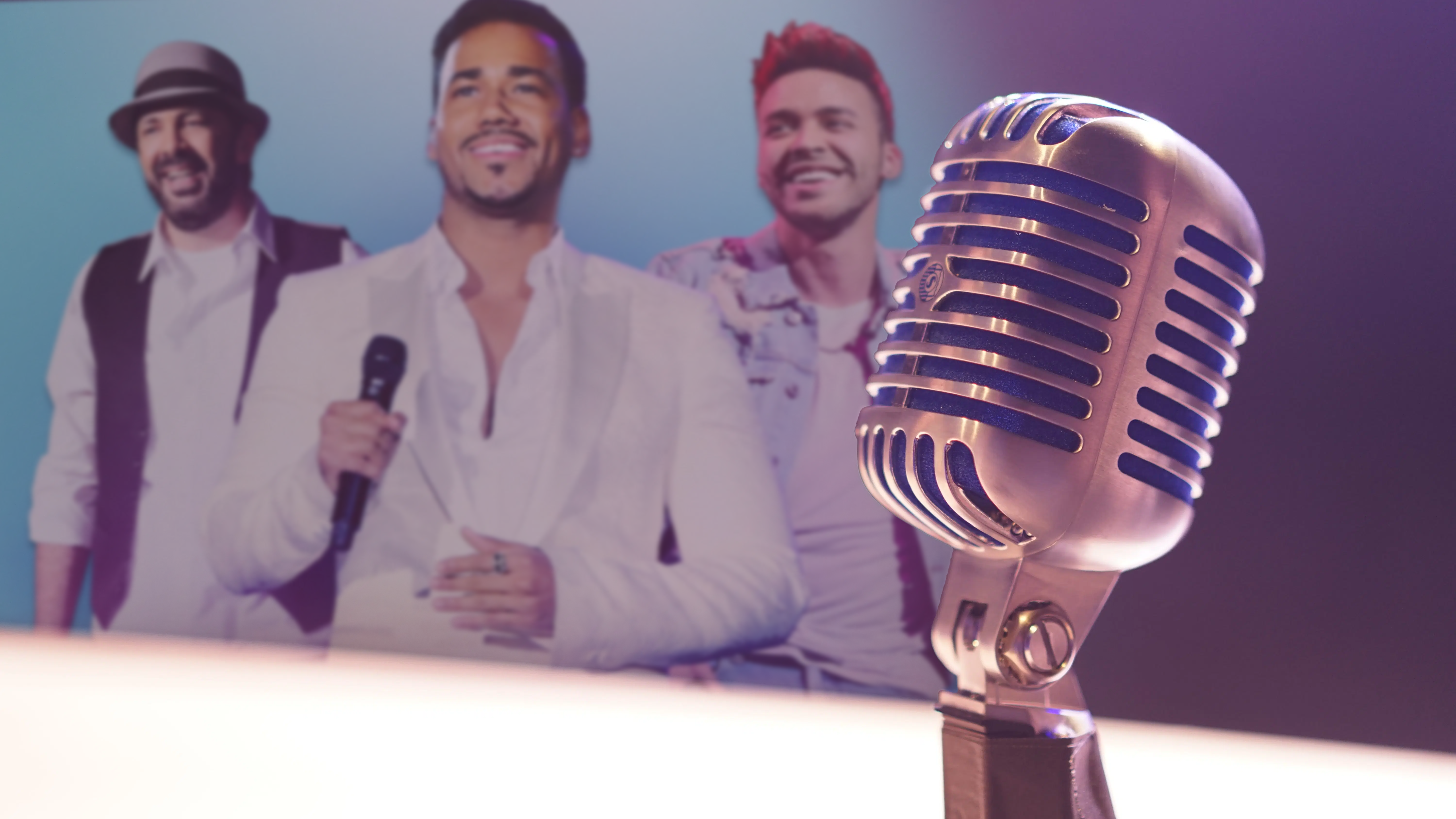 microfono en primer plano con artistas más representativos de la bachata en el fondo
