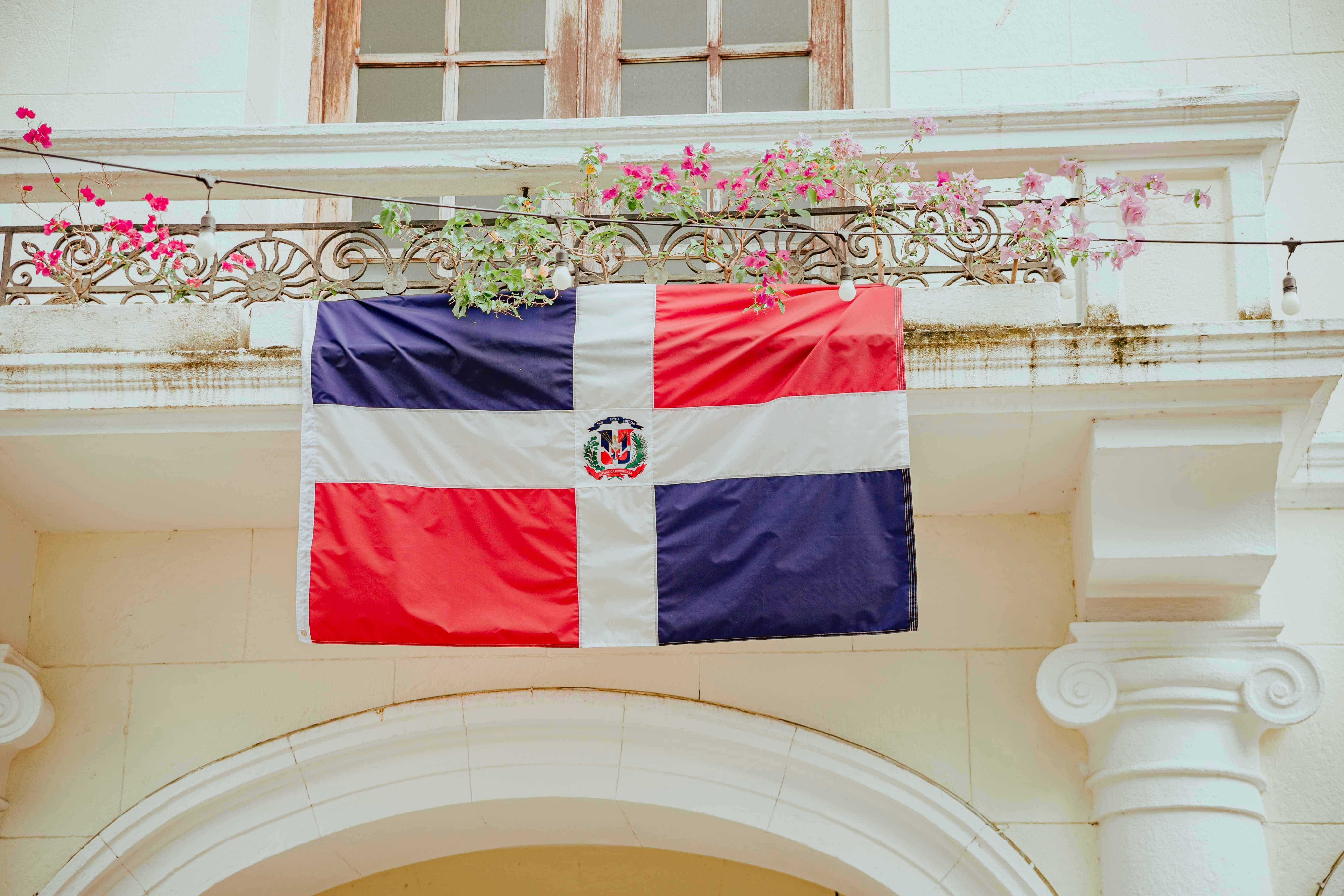 Bandera de República Dominicana colgando en un balcón blanco con flores