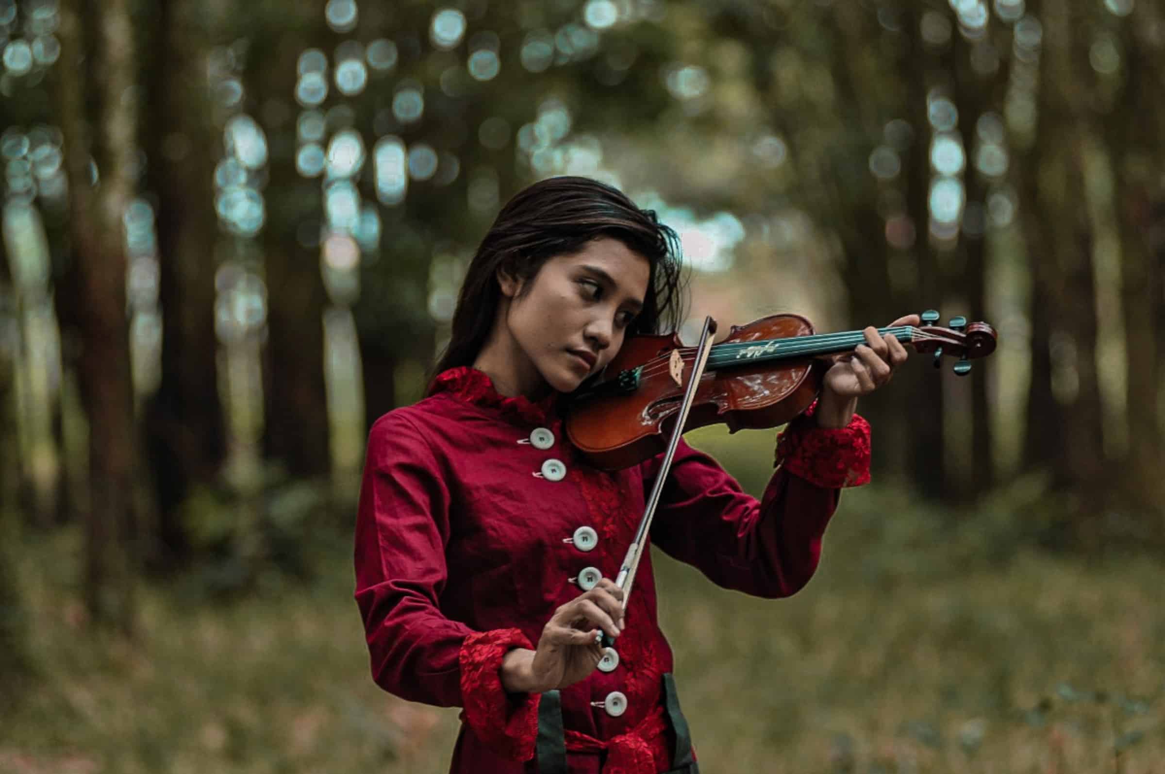 Joven violinista tocando en medio del bosque