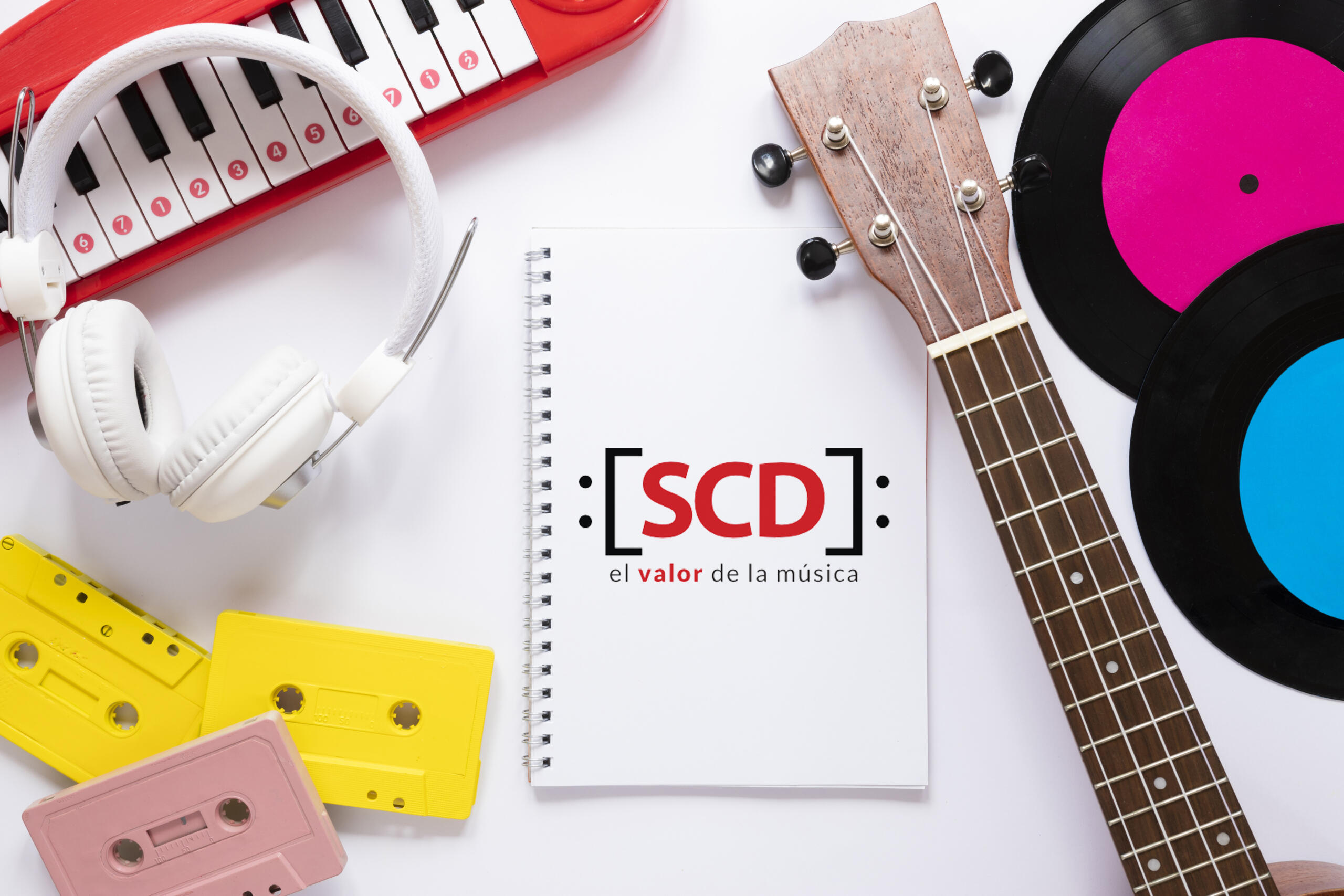 toma cenital de libreta con logo de la SCD con el slogan el valor de la musica rodeado de audífonos, cassets, vinilos y huesillo de la guitarra
