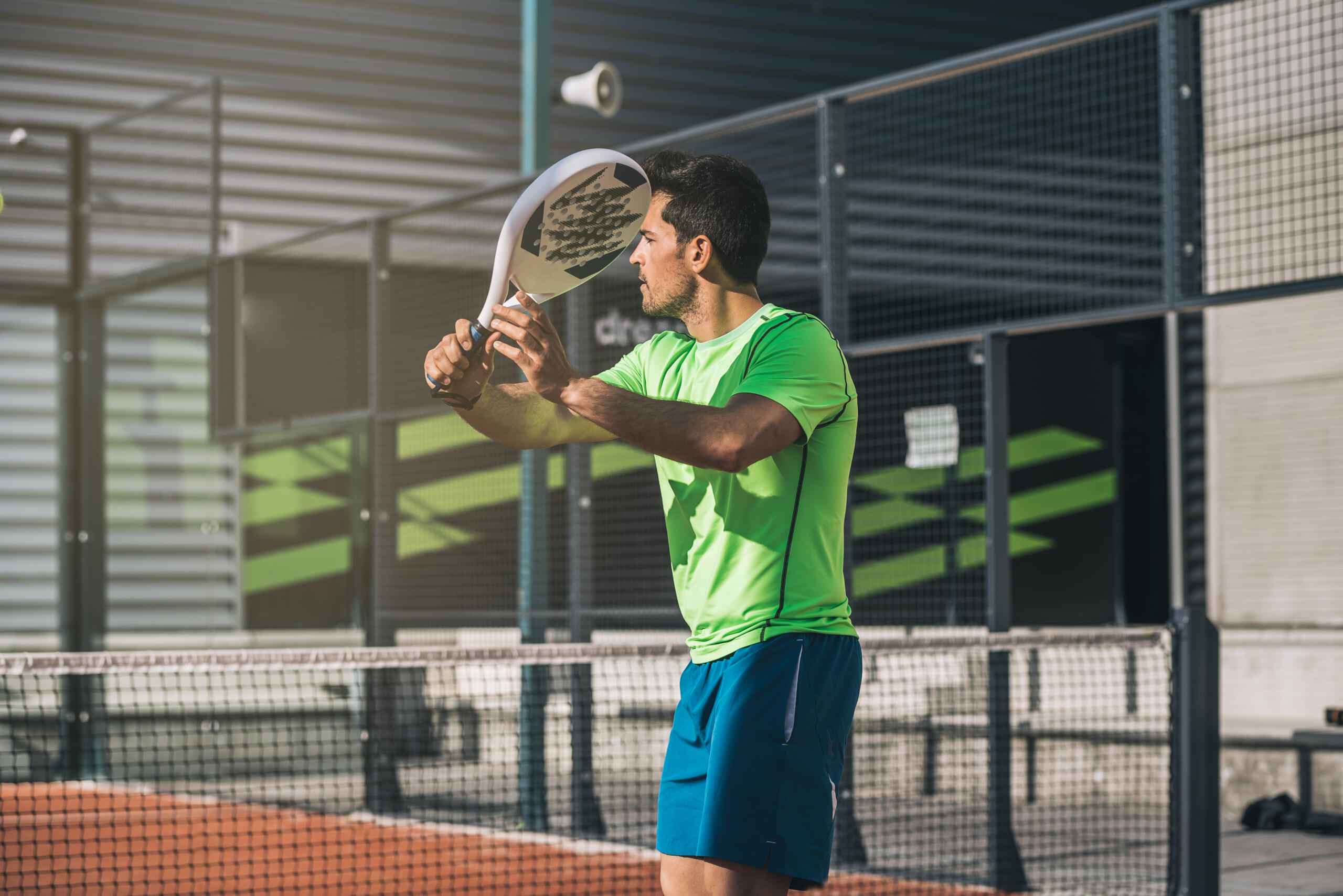 chico en cancha de padel entrenando con la raqueta y polo deportivo verde