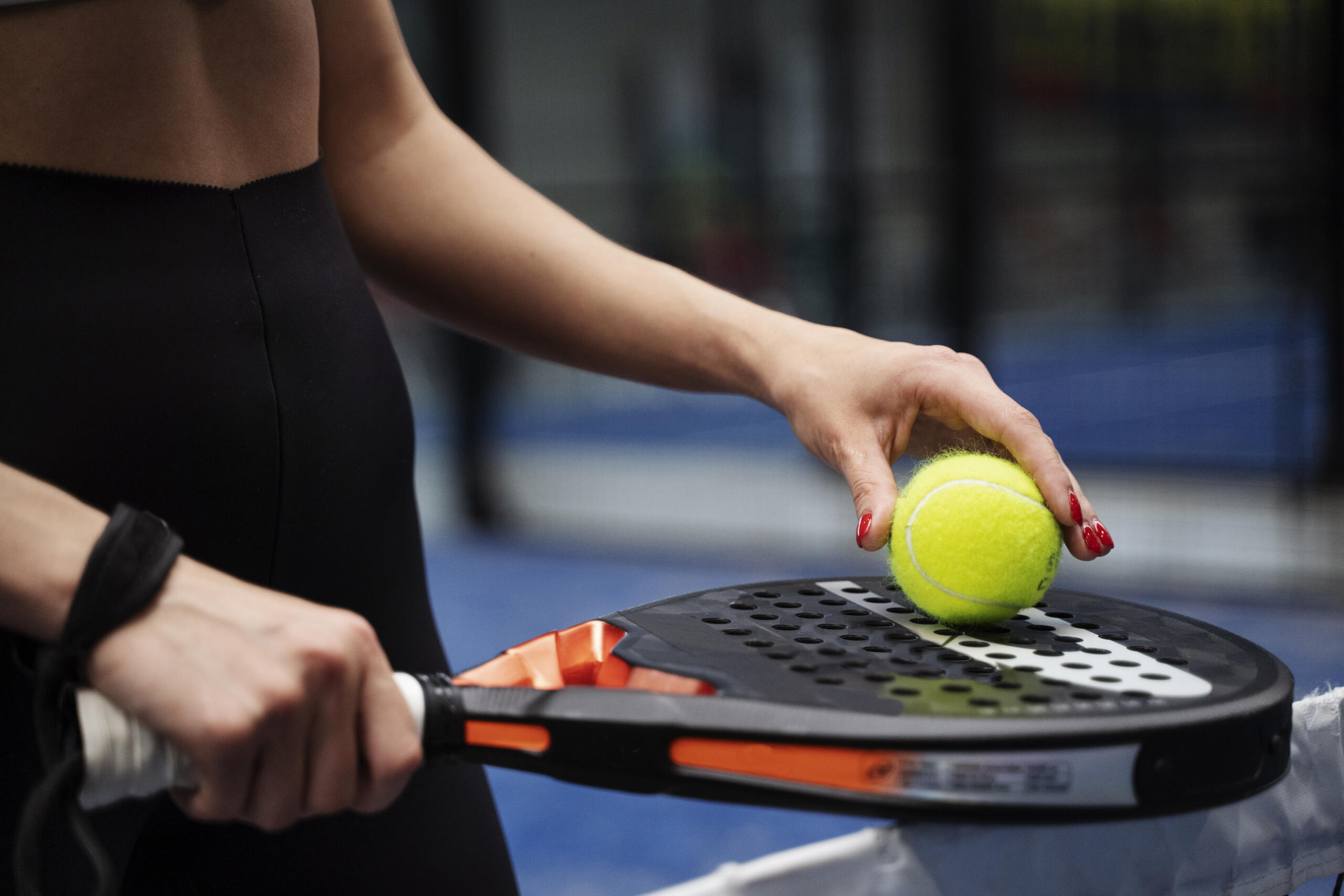 manos de una chica sosteniendo una pelota y raqueta de padel
