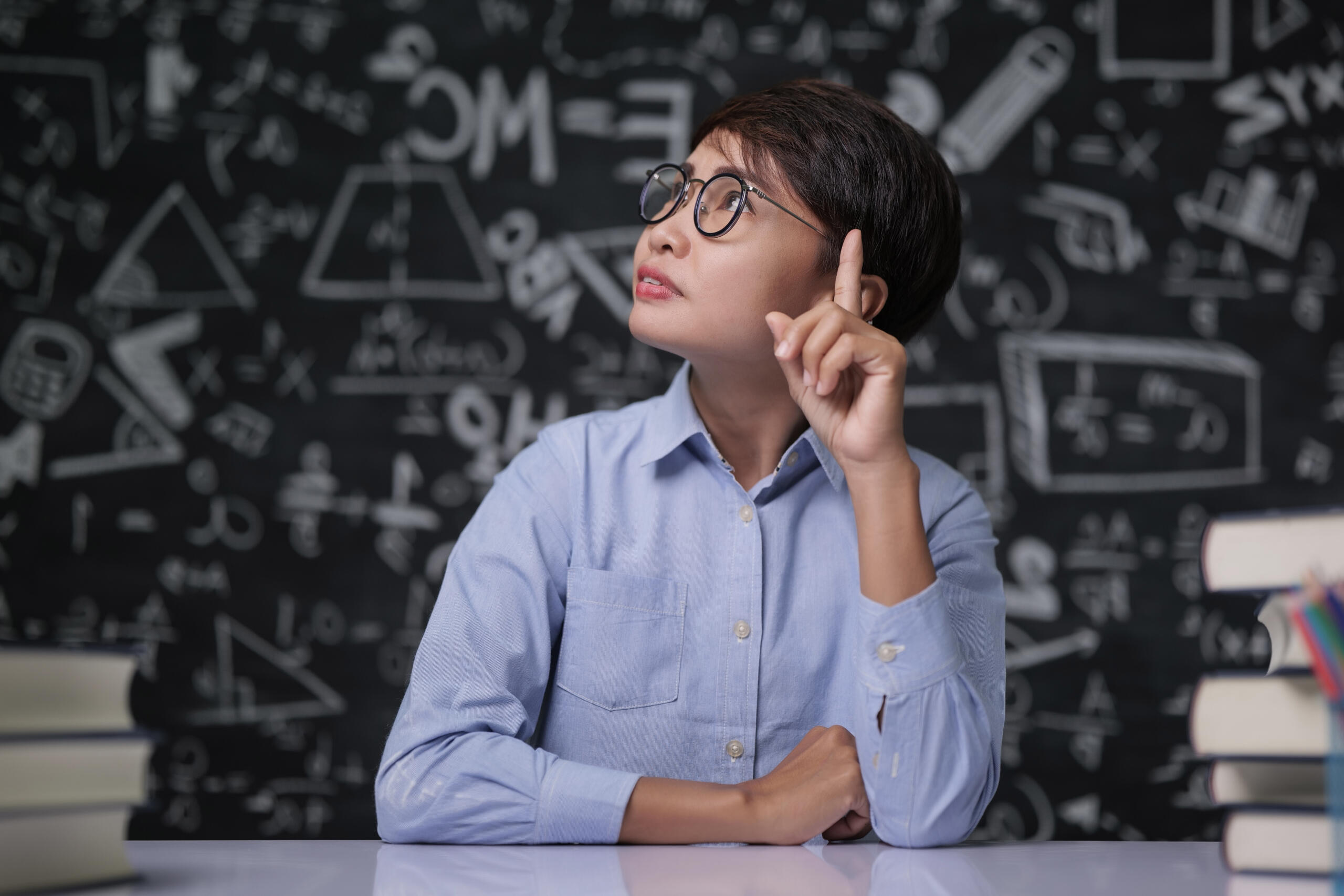alumna pensativa mirando hacia arriba con fondo de pizarra negra llena de operaciones matemáticas