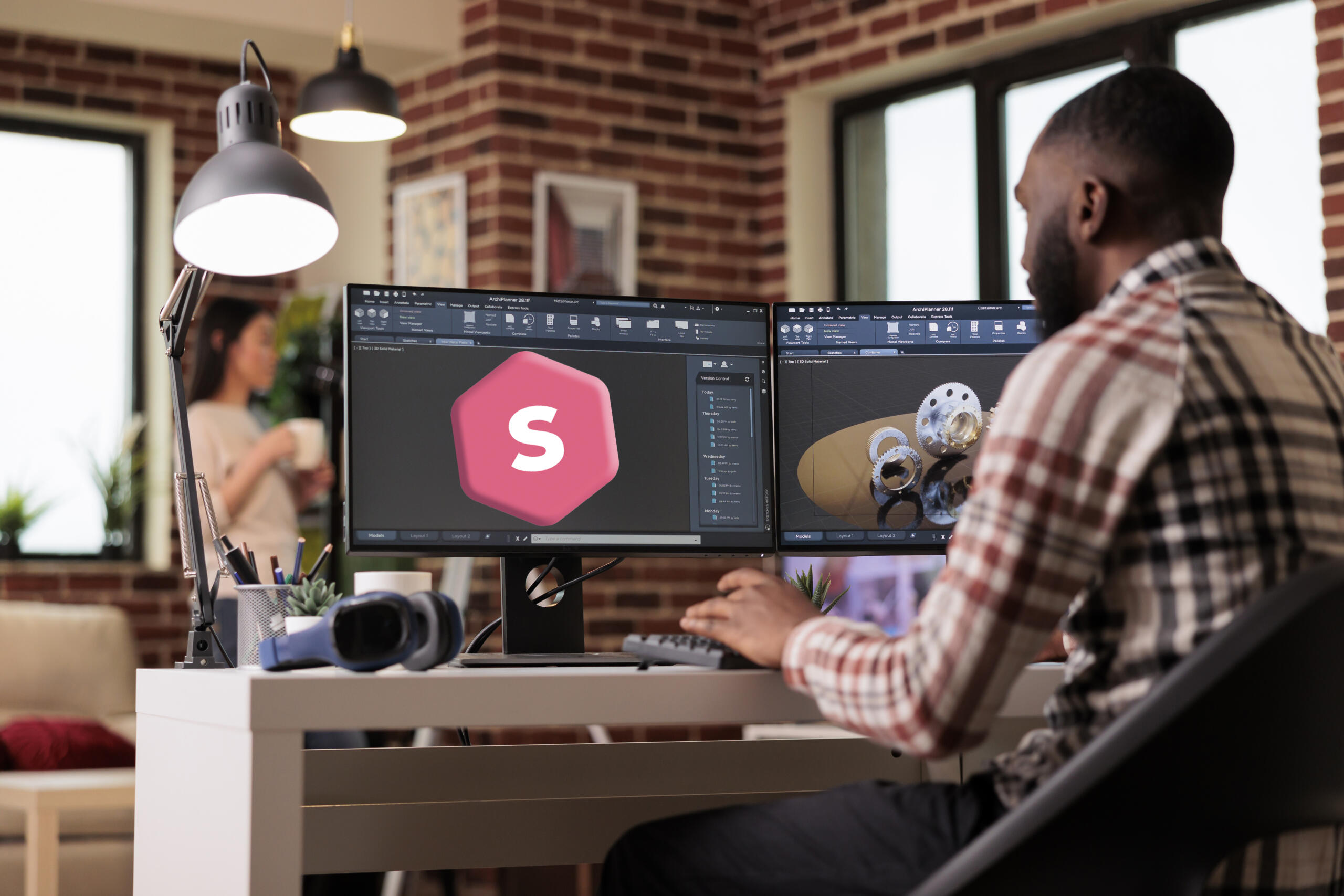 chico de espaldas a la cámara trabajando en un escritorio frente a sus dos monitores un modelado 3d con logo de superprof y modelo industrial
