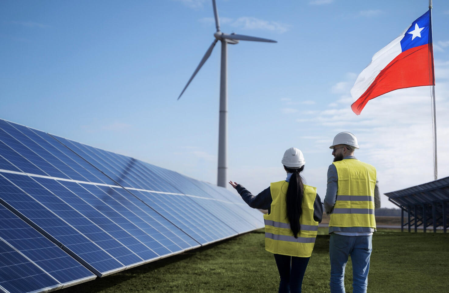 planta de hidrógeno verde con dos trabajadores recorriendo el campo y una bandera de Chile en asta al lado derecho de la imagen