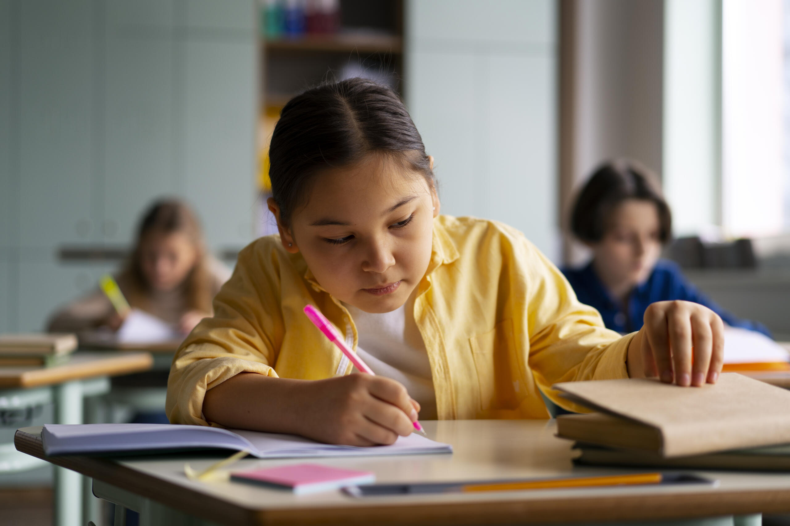 niña en carpeta de colegio escribiendo entre sus cuadernos con un lapicero rosa
