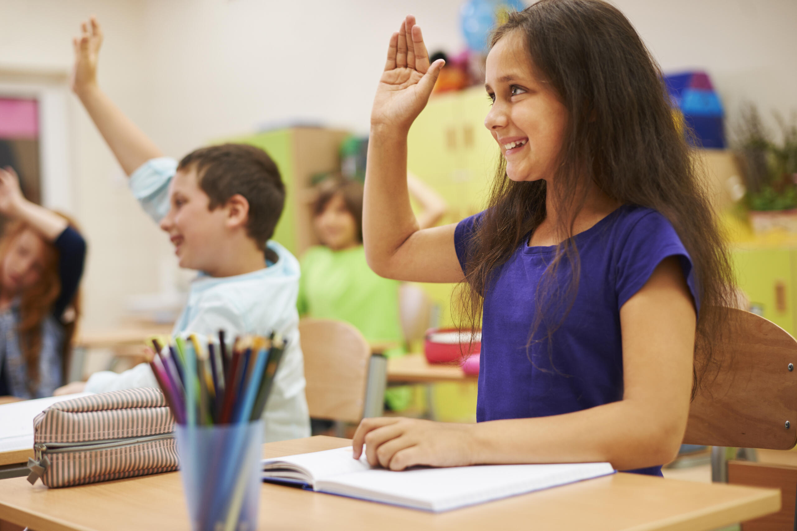 niños sonrientes levantando la mano en un aula de clase