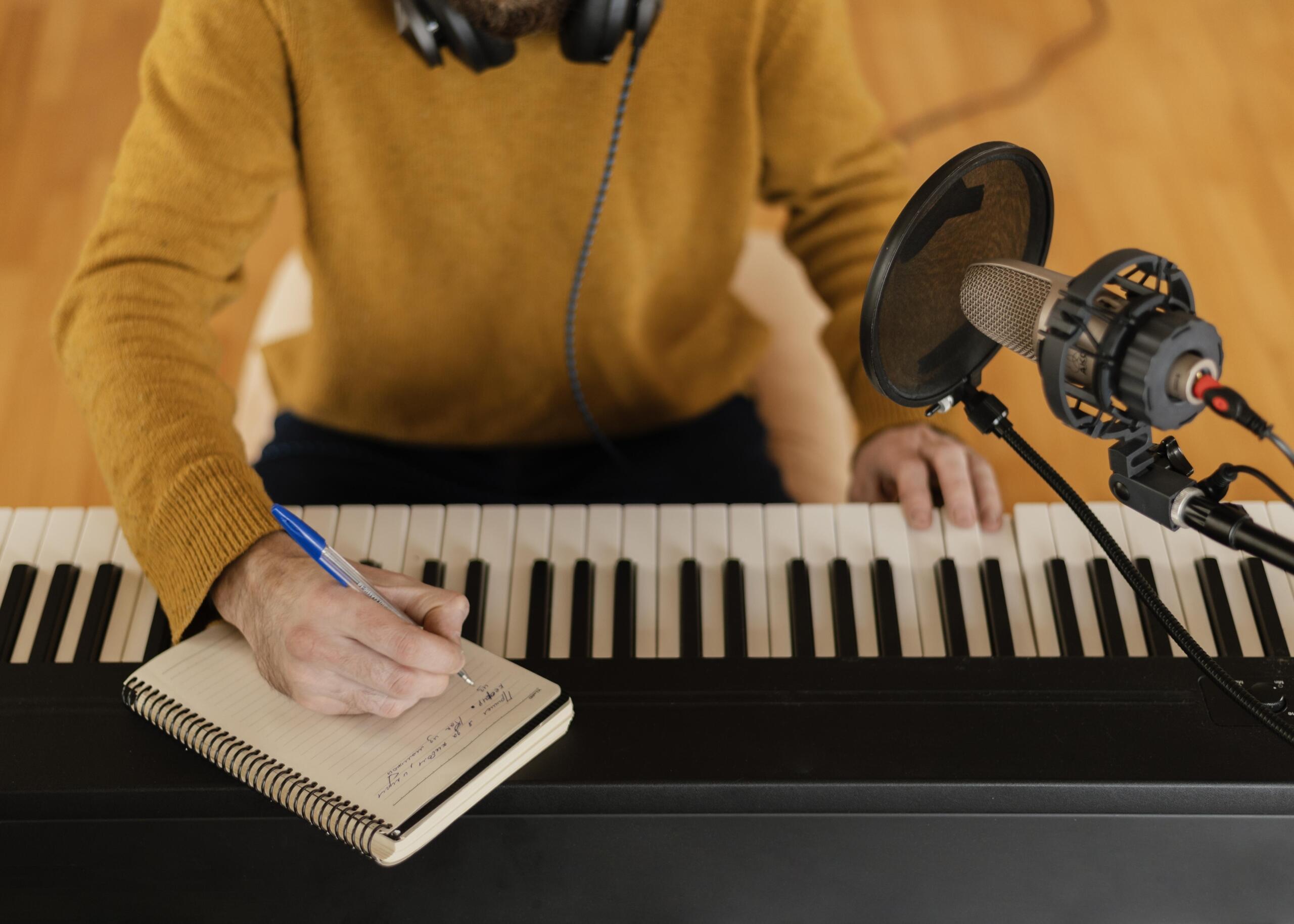 toma cenital a detalle en manos de un chico anotando en una libreta mientras graba una canción con su teclado.
