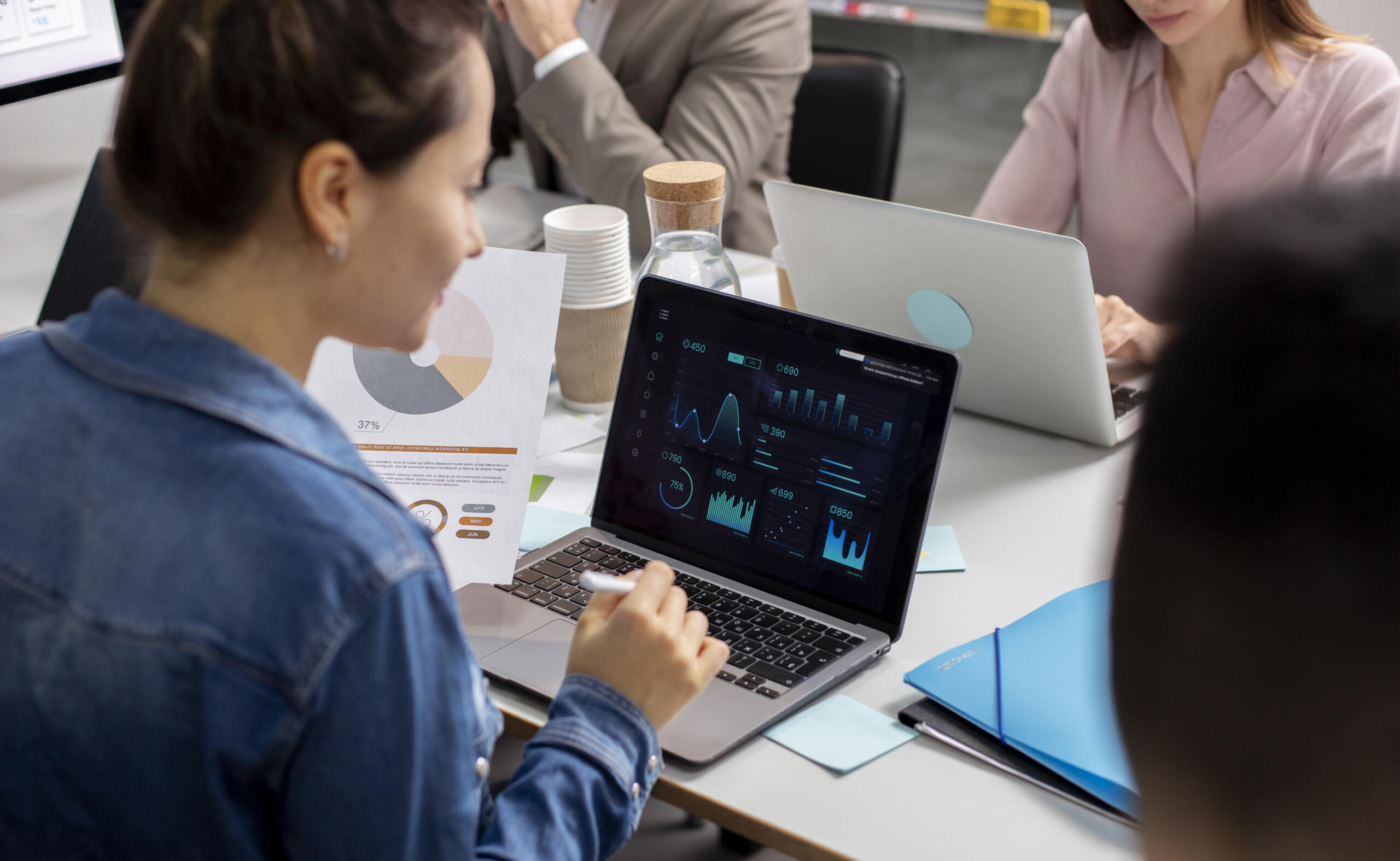 toma de un equipo de trabajo con foco en una chica revisando un reporte analytics en la pantalla de su laptop