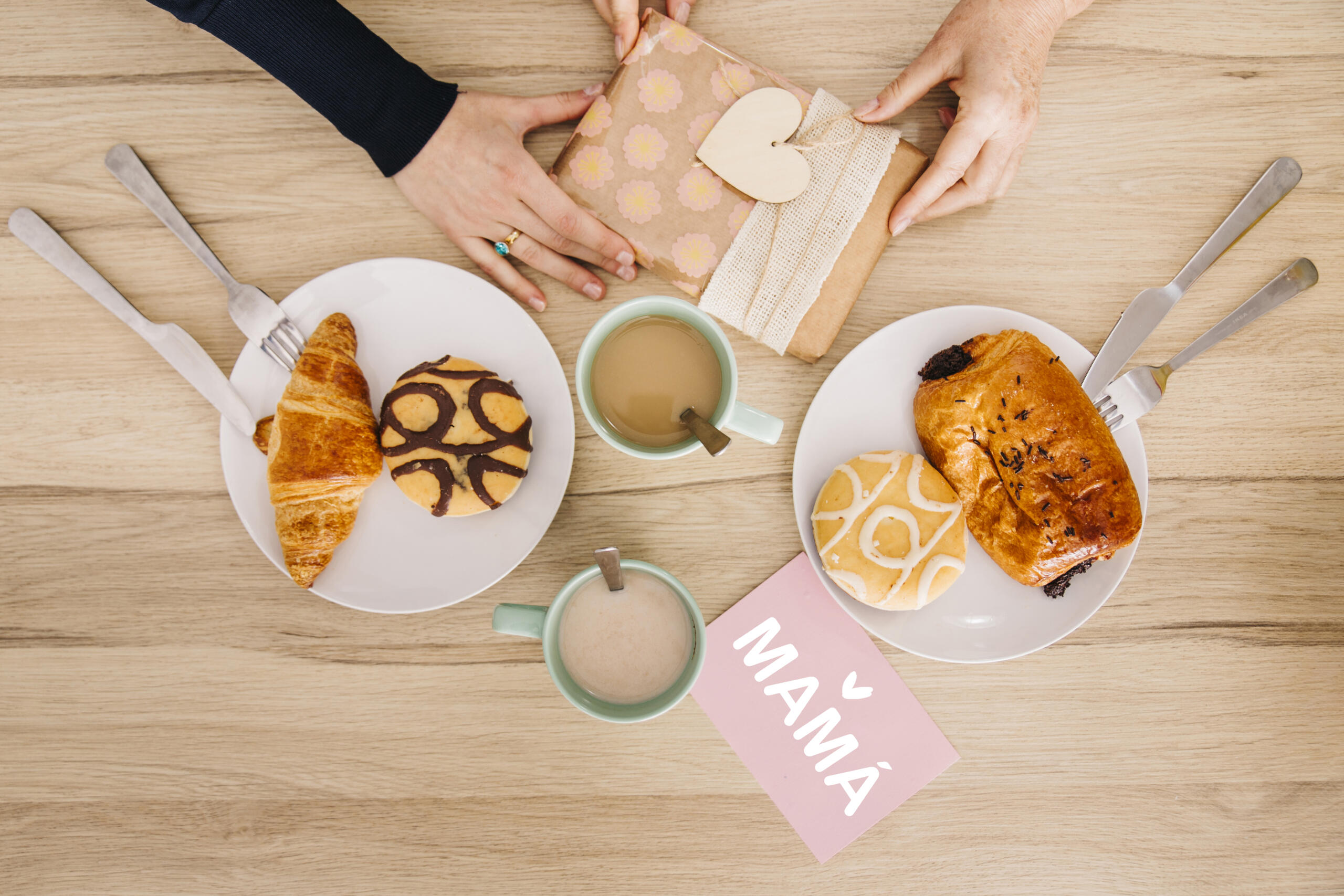 toma cenital de una mesa de desayuno por el dia de la madre y dos manos entregándose un regalo