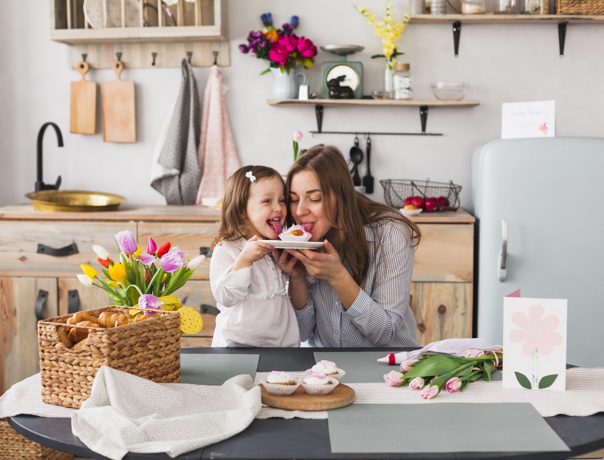 mamá y niña pequeña sosteniendo un plato con un cupcake y sacando la lengua sonrientes como si lamieran el postre a la vez