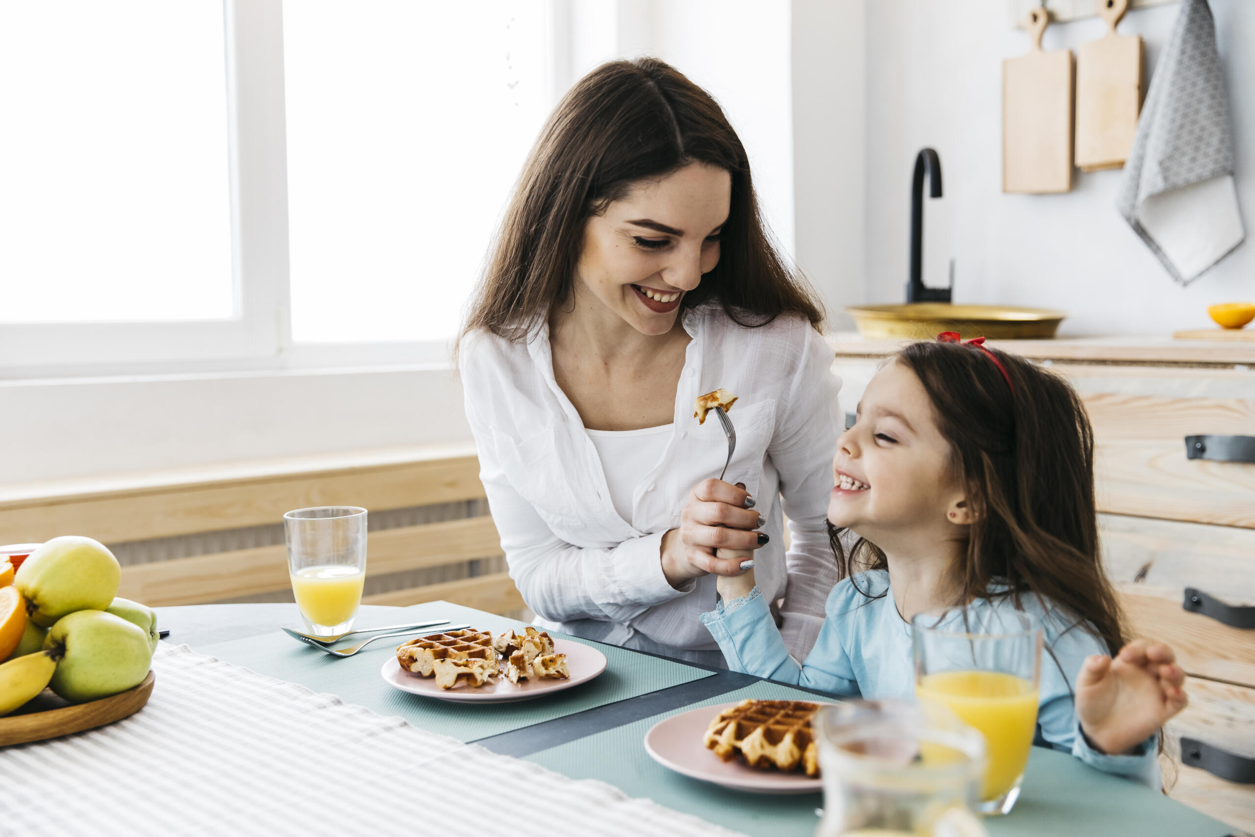 toma de una mamá e hija sonrientes compartiendo unos waffles en la cocina