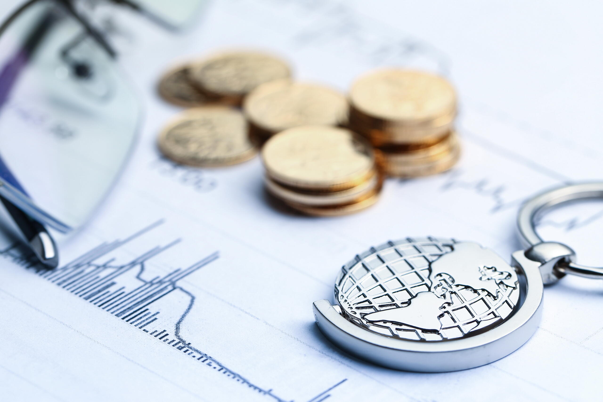 toma detalle de un llavero de mundo sobre unas hojas estadísticas y monedas