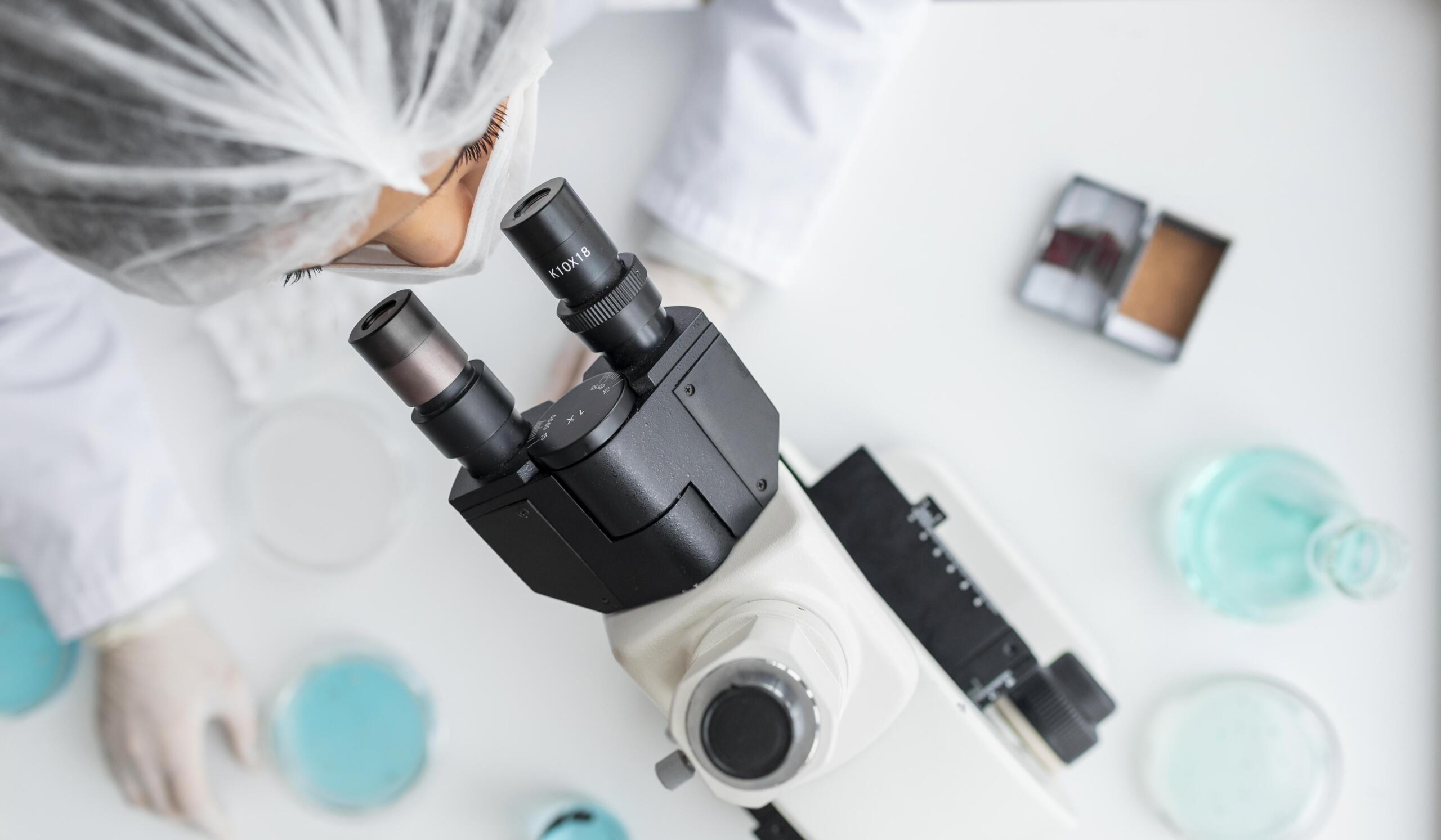 Toma cenital de una doctora mirando muestras a través de un microscopio