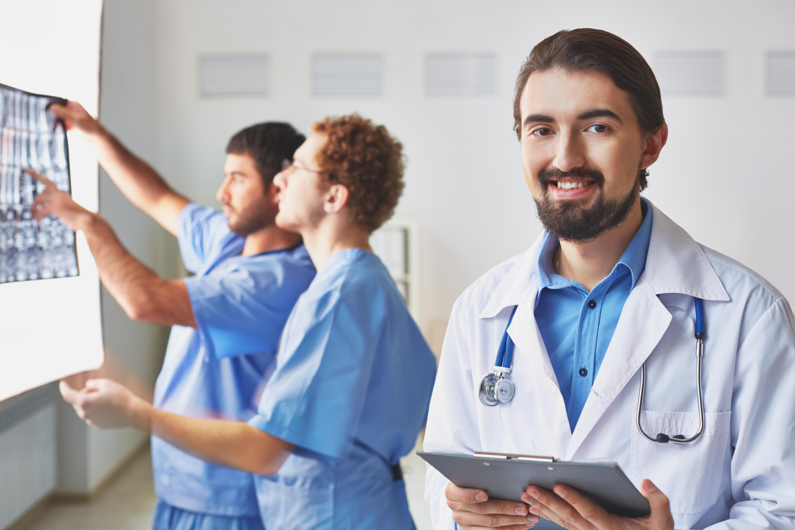 Doctor sonriente en primer plano con dos médicos en el fondo revisando unas radiografías.