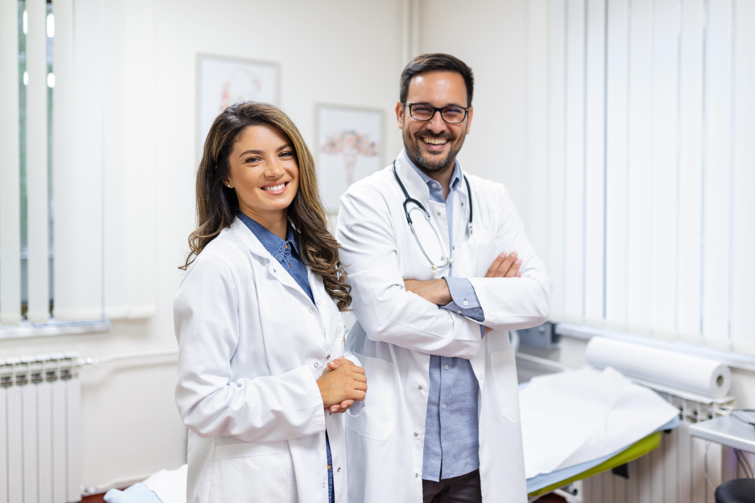 Dos doctores sonrientes mirando a la cámara en medio de un consultorio